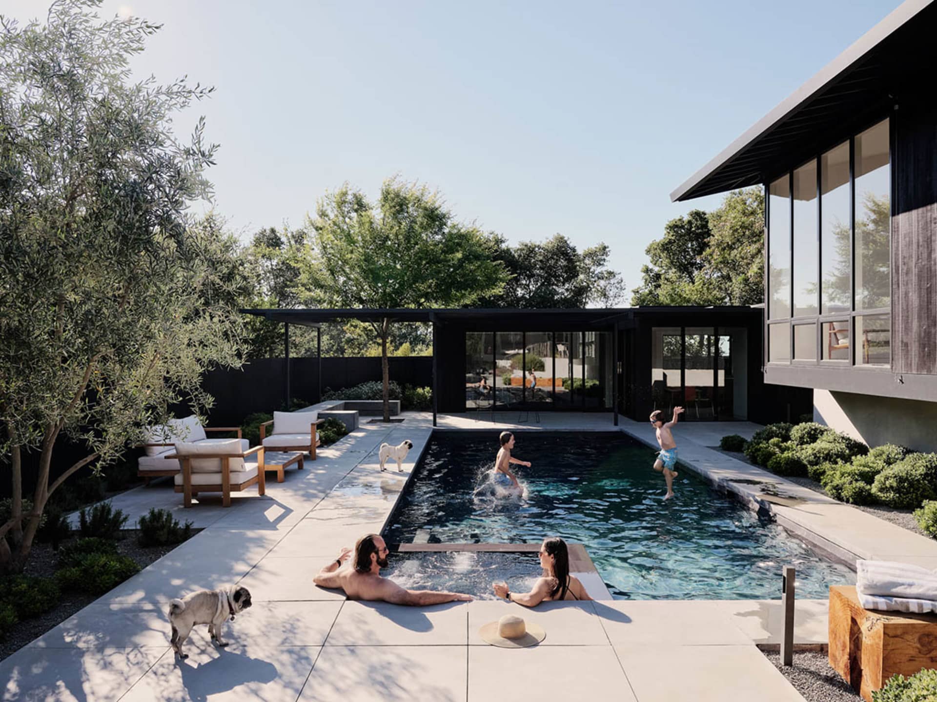 A family is enjoying a modern poolside gathering on a sunny day surrounded by concrete and brownstone.