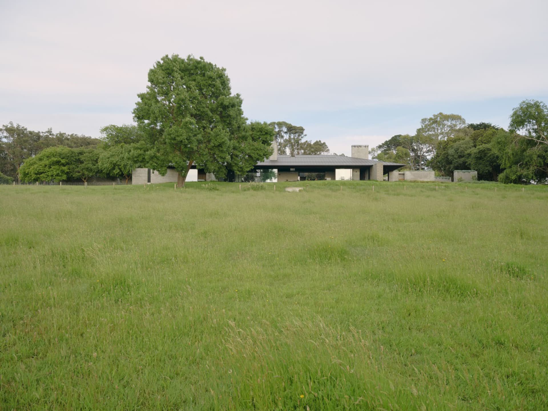 一座現代住宅，坐落於青草地中，展現混凝土與玻璃元素