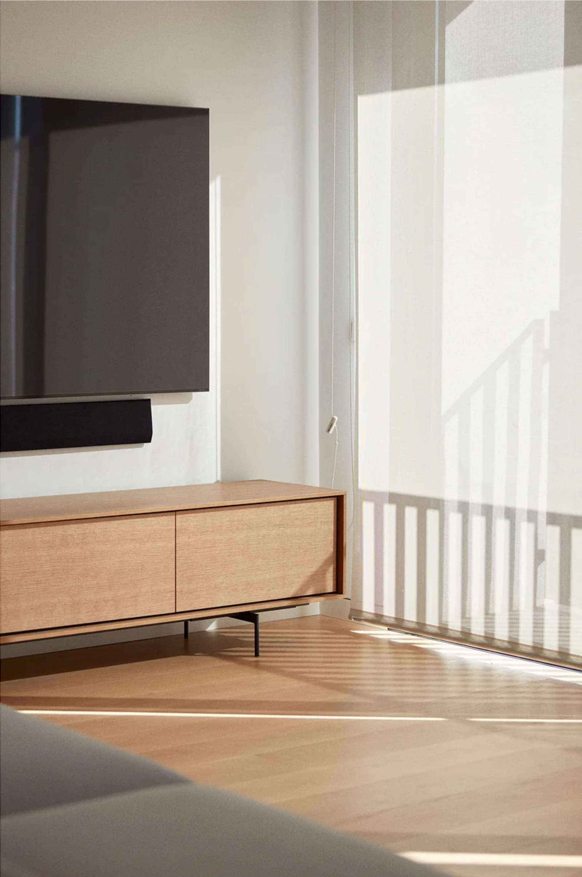 Modern minimalist living room with wooden cabinet and sunlight streaming through the window.