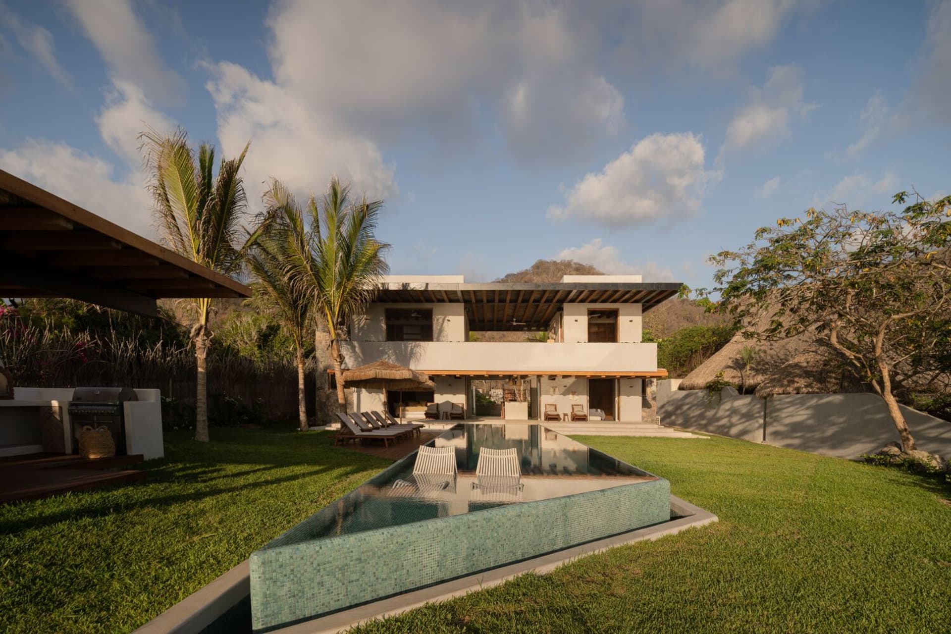 An elegant modern house featuring concrete and wood exteriors with a large swimming pool and lush garden.
