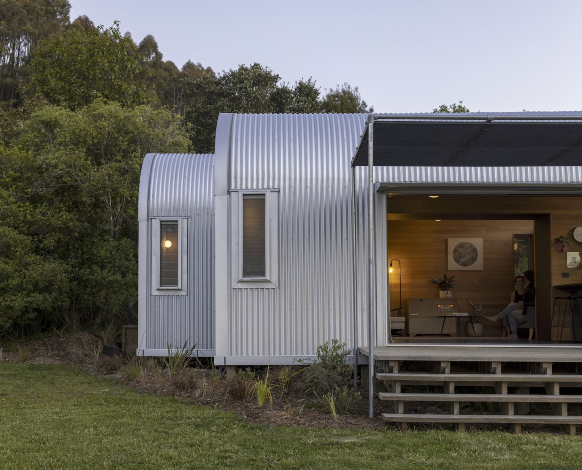 A contemporary metal-clad residential extension with a corrugated roof, large windows, and a serene outdoor setting.