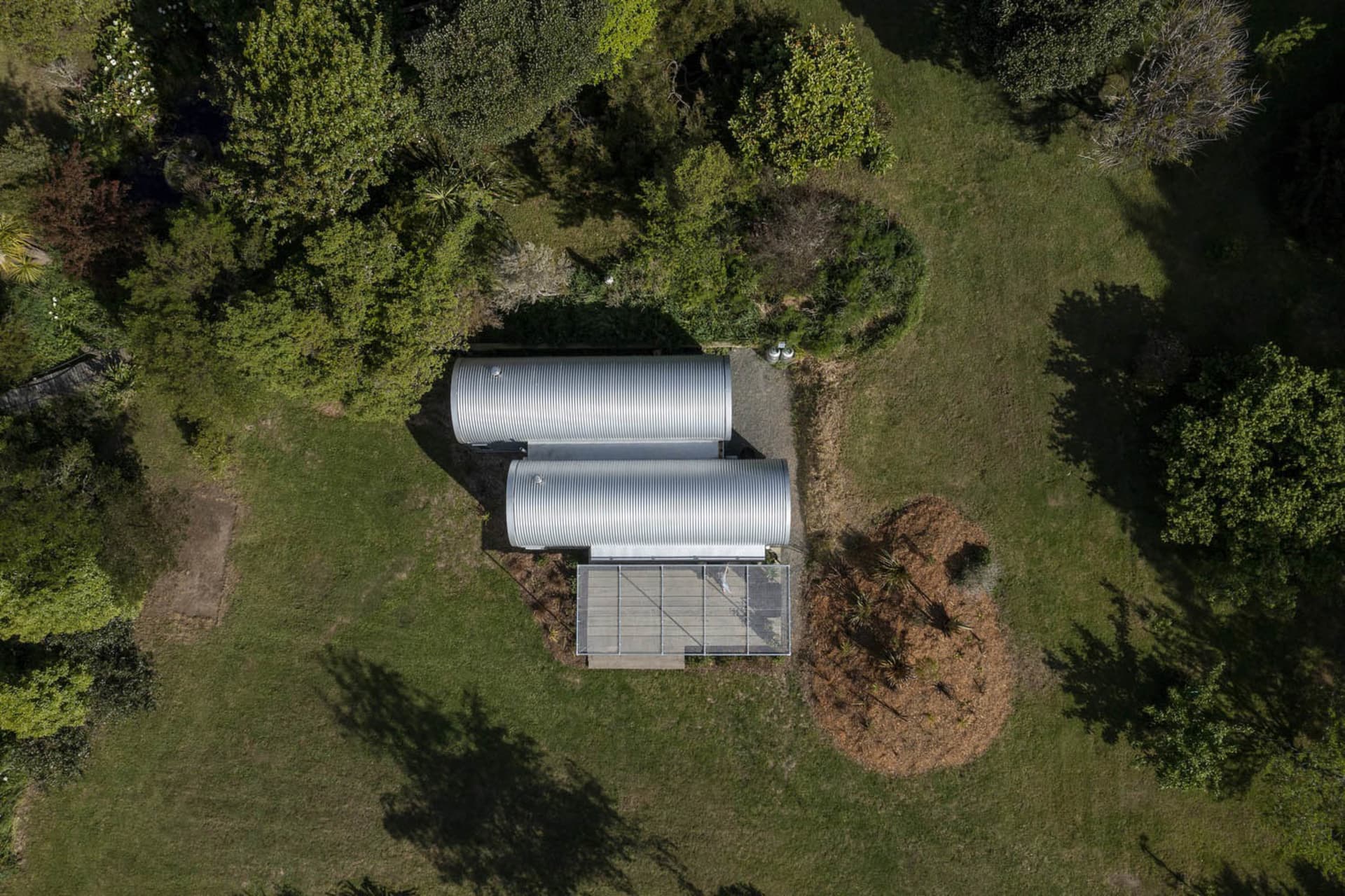 Aerial view of a minimalist house with a corrugated metal roof surrounded by greenery.