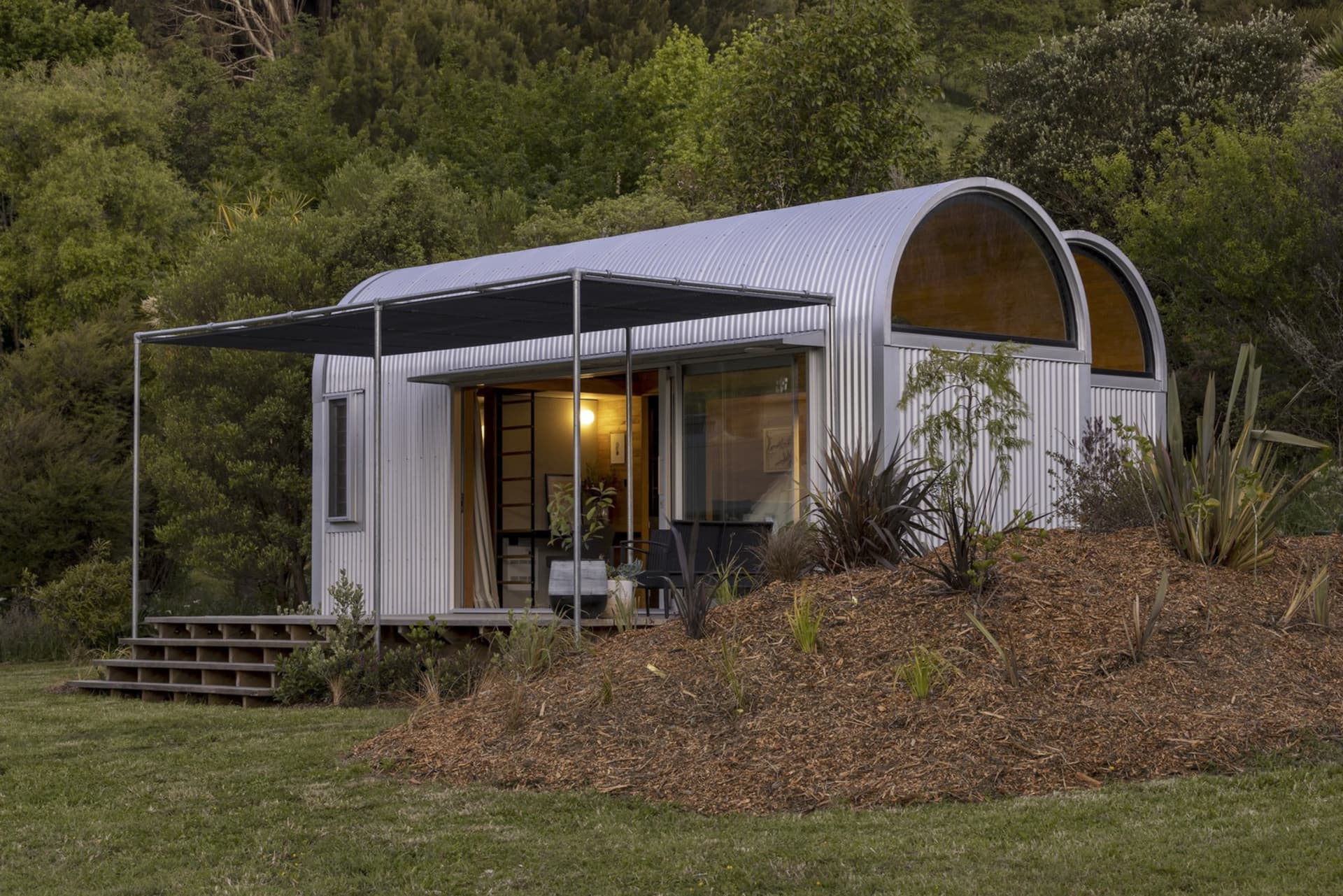 A metal studio hut with a curved roof nestled in a forested area.