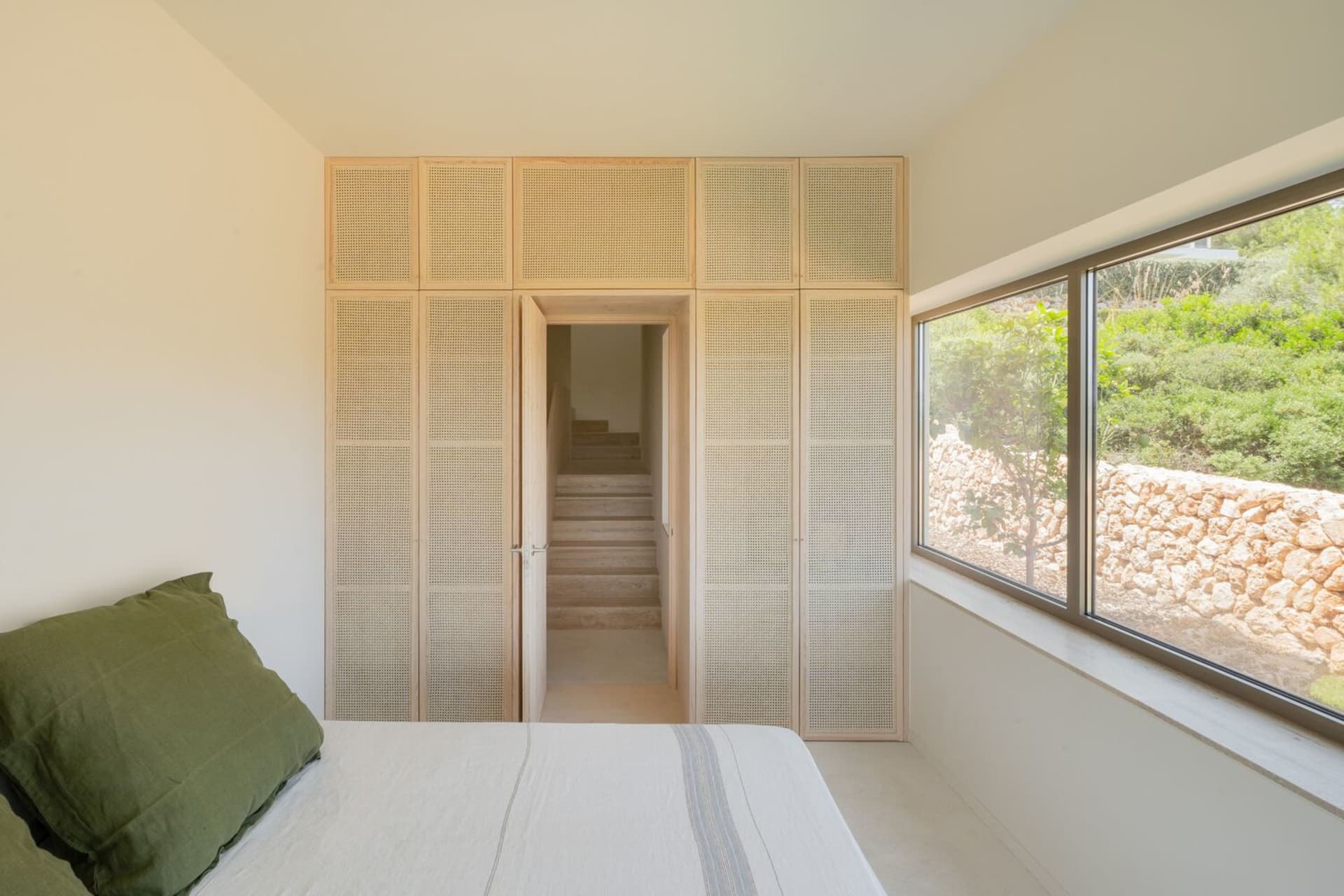 Minimalist bedroom featuring wooden furniture and a large window overlooking greenery.
