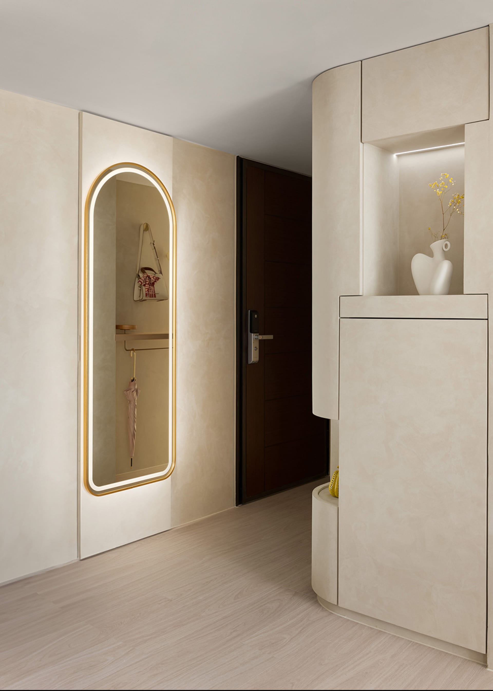 Modern entrance hallway with neutral-toned walls, floor, and furniture, featuring an arch-shaped mirror and a storage unit wi