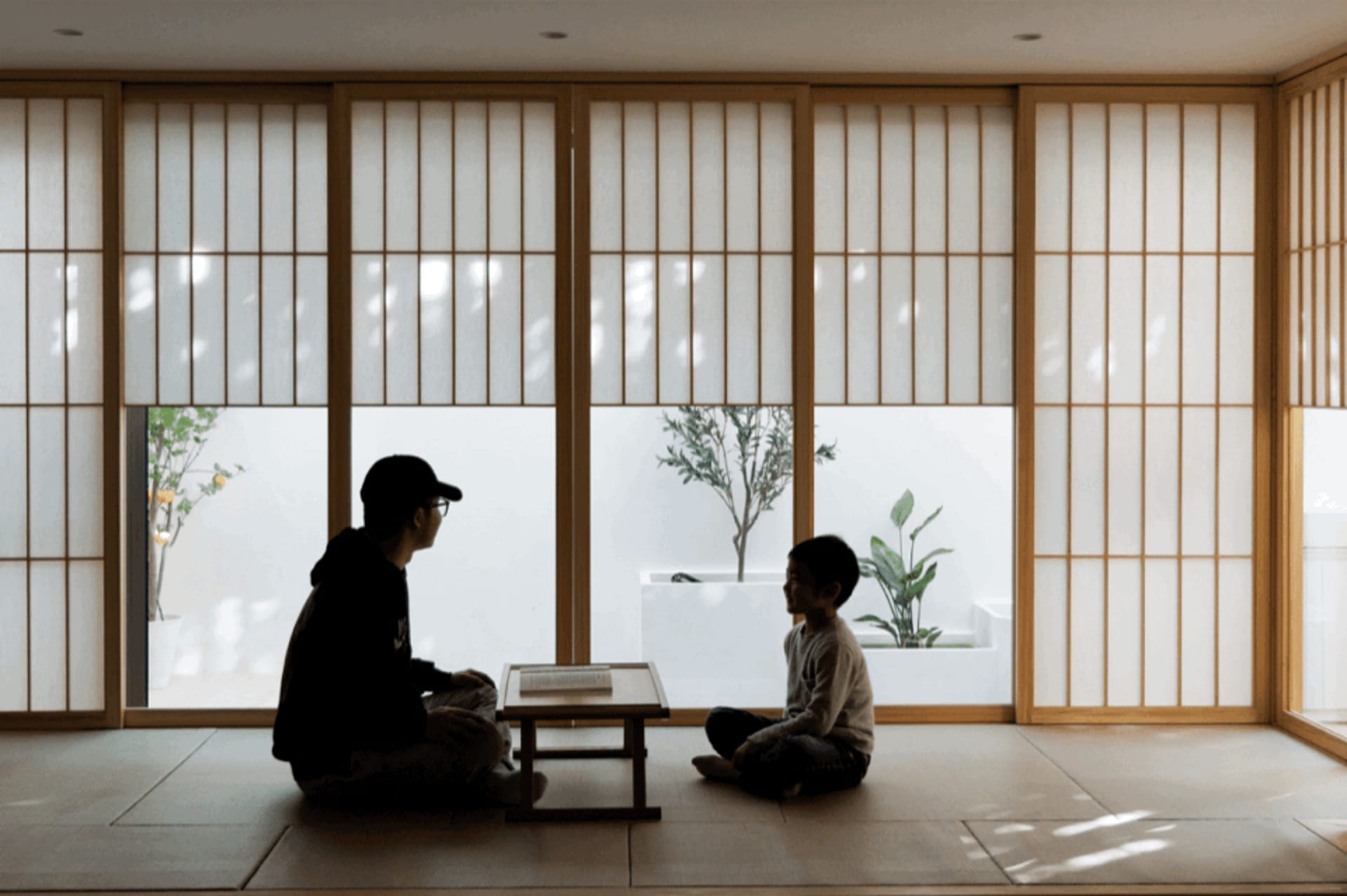 Two people in silhouette sitting in a room with wooden sliding doors and a plant in the background.