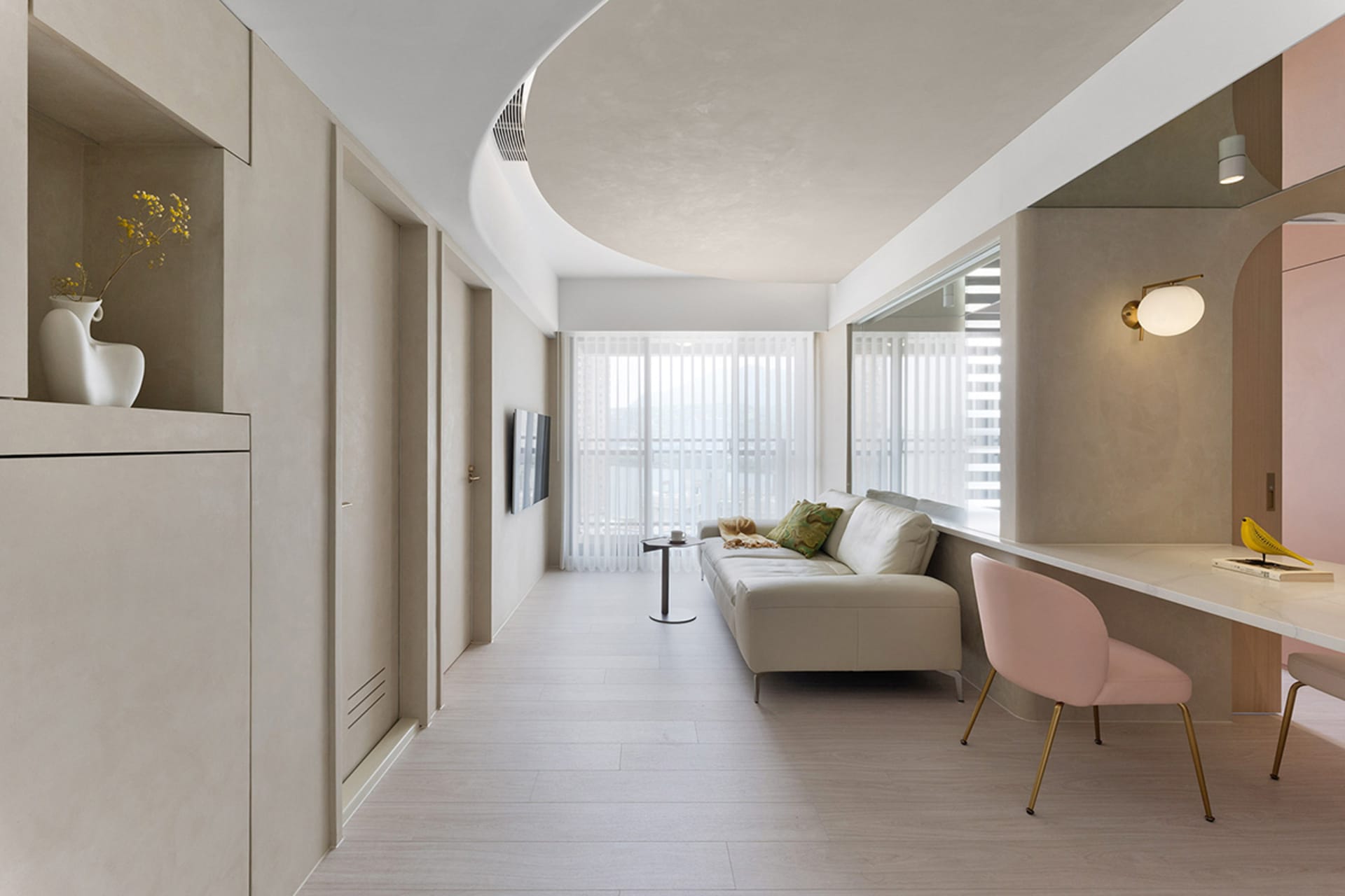 A minimalist living room with concrete walls, a white sofa, and a pink chair.