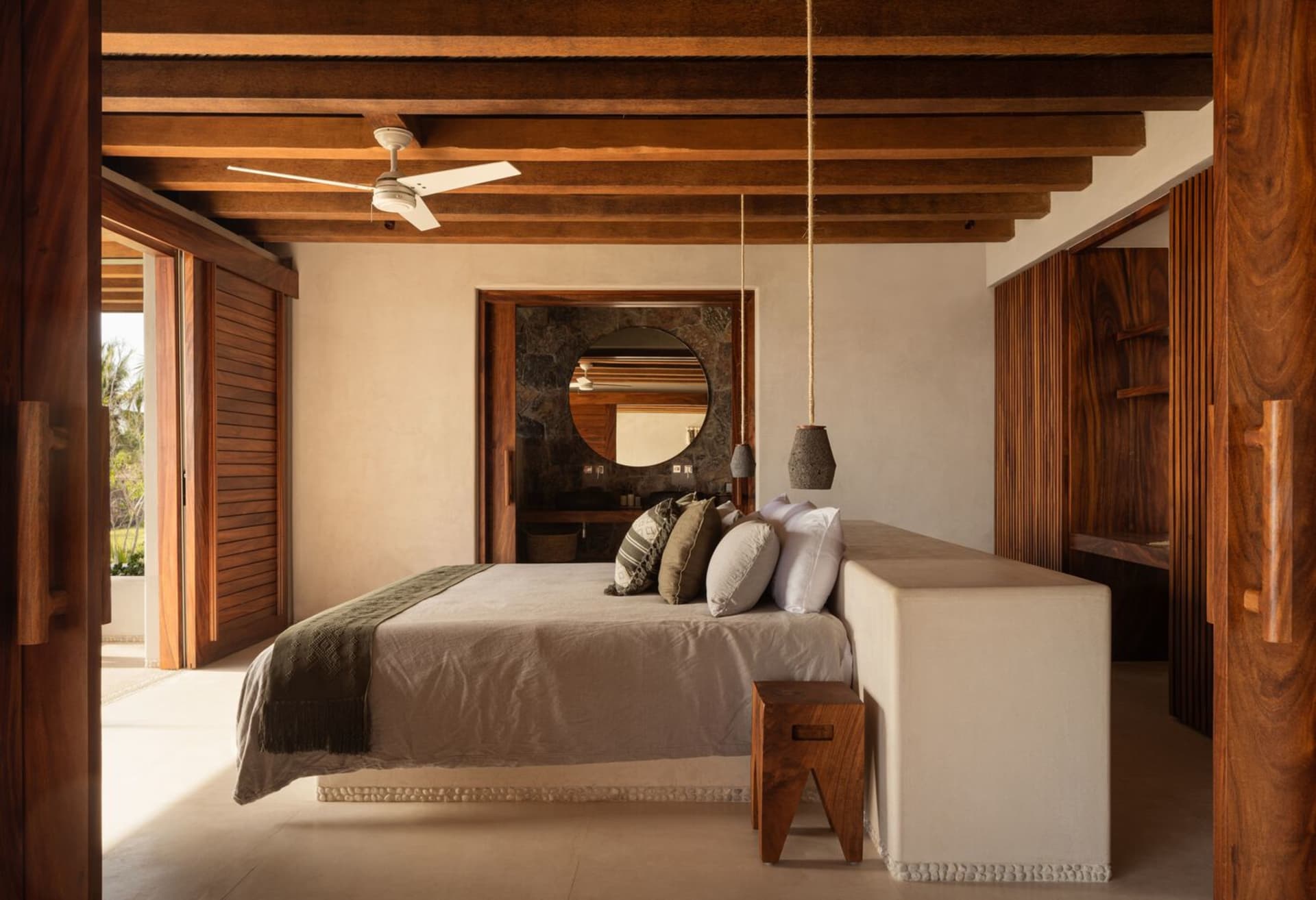 A minimalist bedroom with a low bed, wooden flooring, and a ceiling fan.