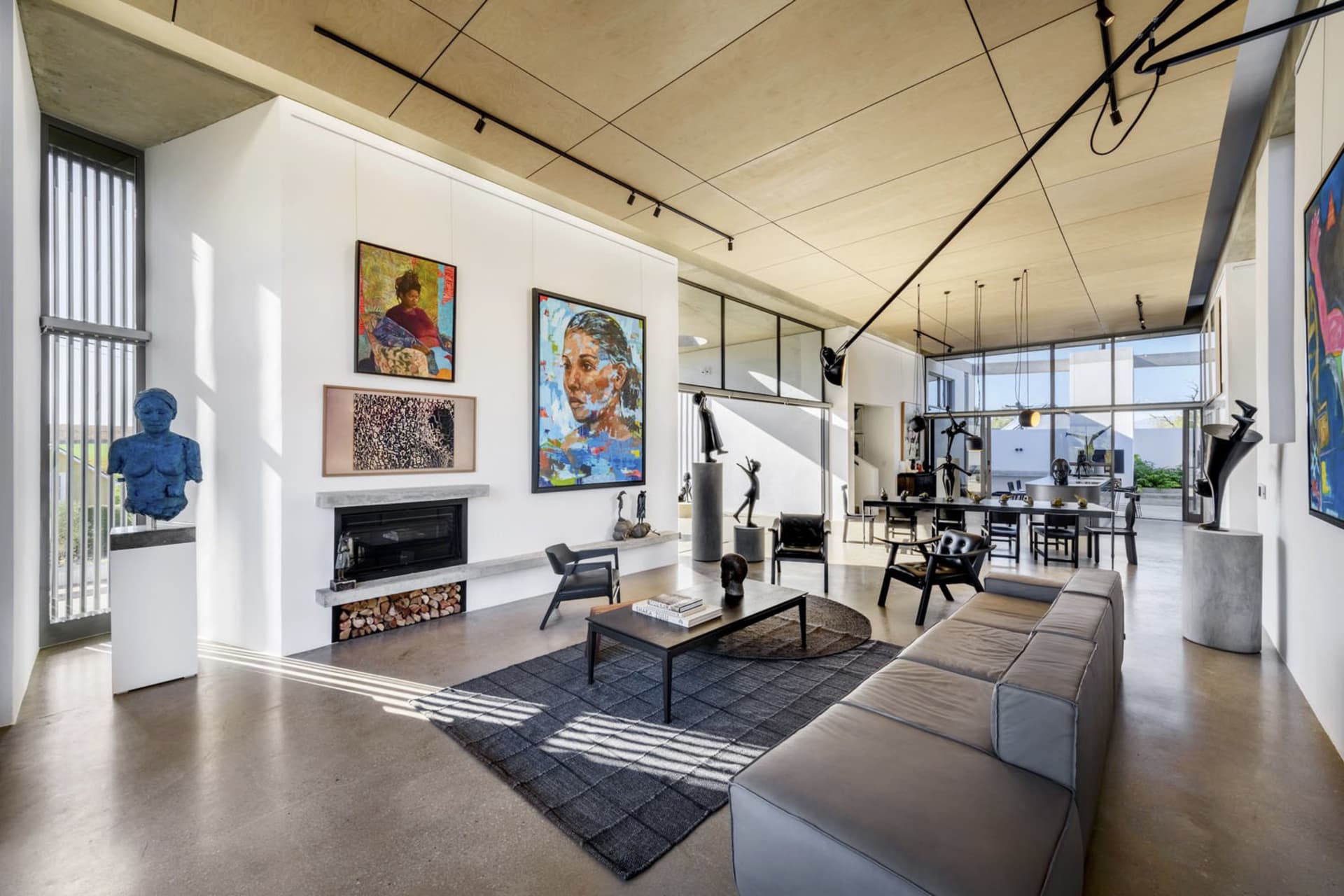 Modern minimalist living room with concrete walls and floor, featuring a large sofa, coffee table, fireplace, and abstract ar