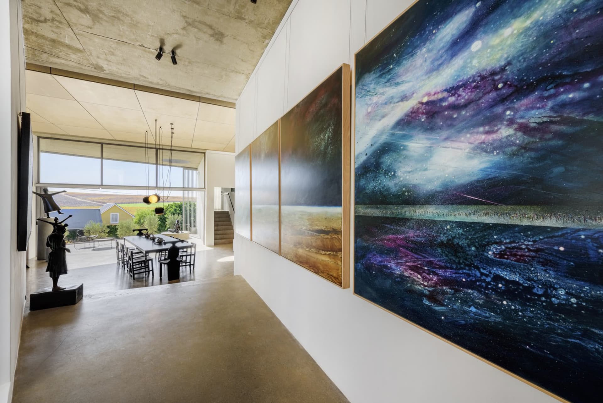 A spacious gallery with modern art installations, including a large cosmic painting and sculptures.