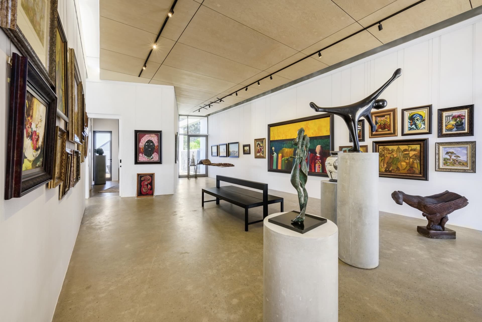 Modern art gallery with sculptures on concrete pedestals, metal figures, and paintings on the walls.