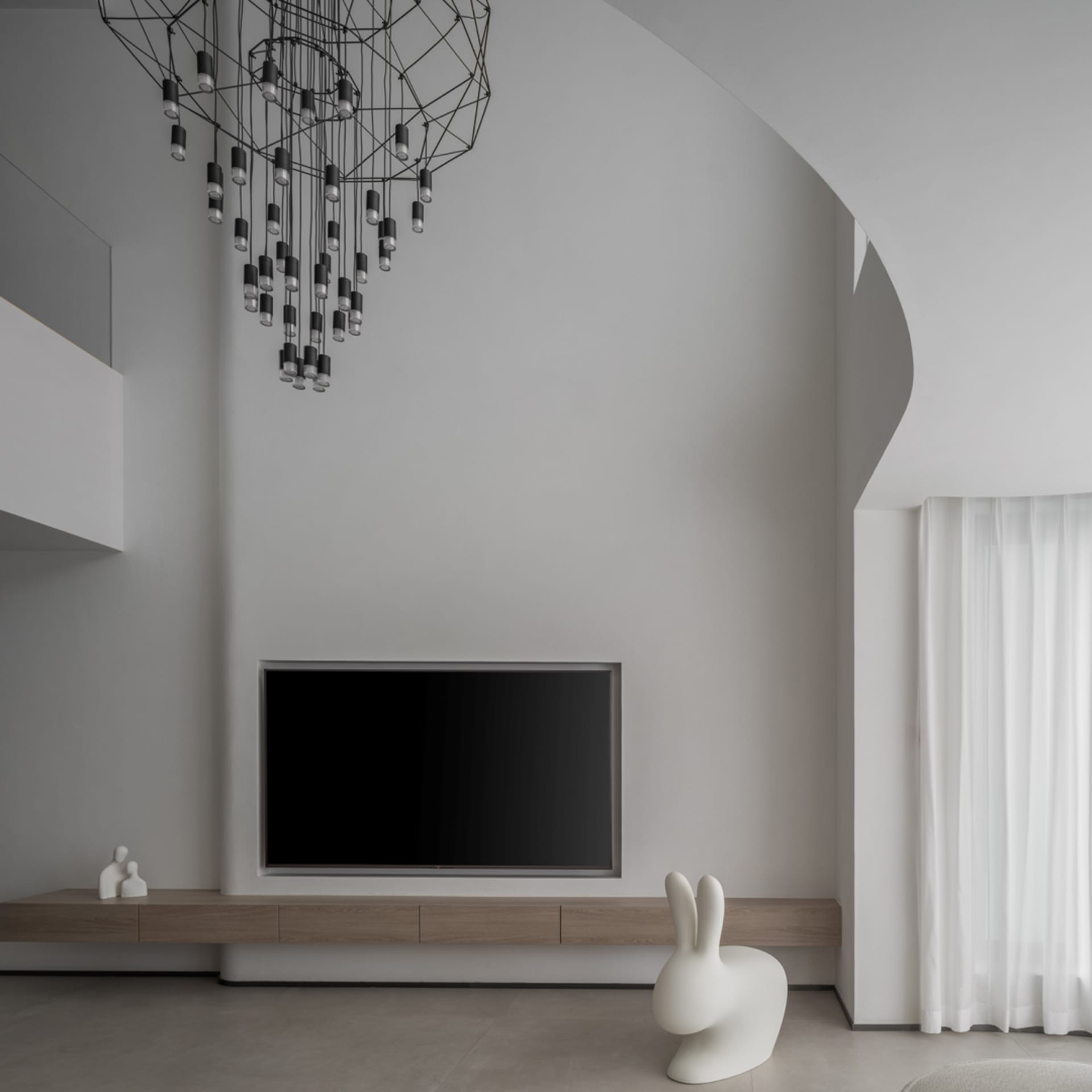 Modern minimalist living room featuring wood, concrete, and glass materials and a geometric chandelier hanging above.