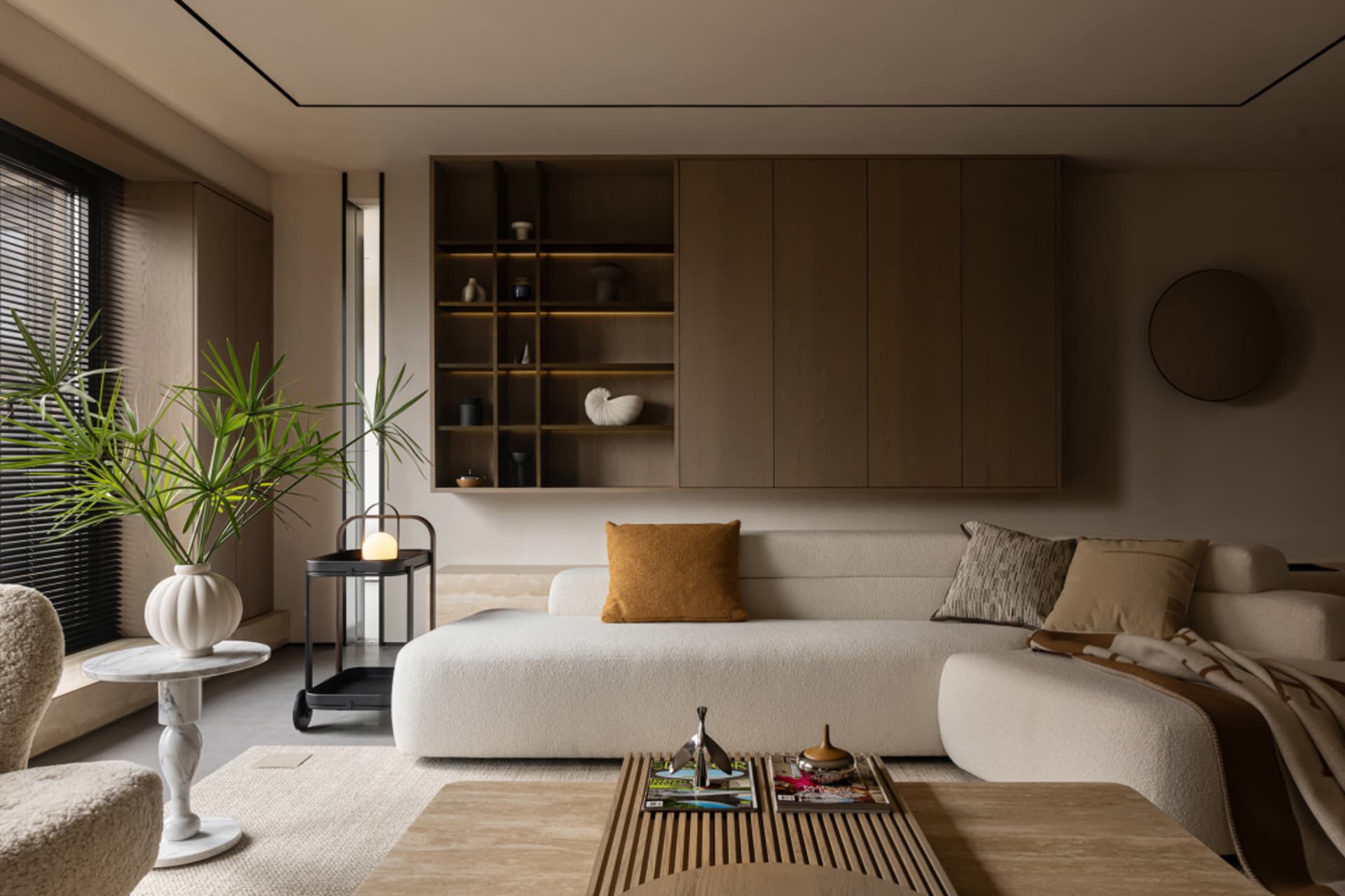 A modern living room with a minimalist design, featuring neutral-toned furniture, a large window, a coffee table with magazin
