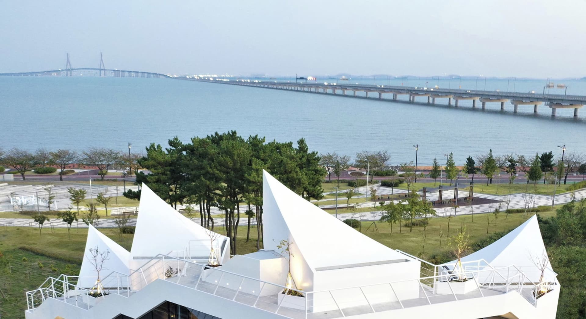 現代公園展示混凝土步道、綠意植栽,以及背景中的橋樑。