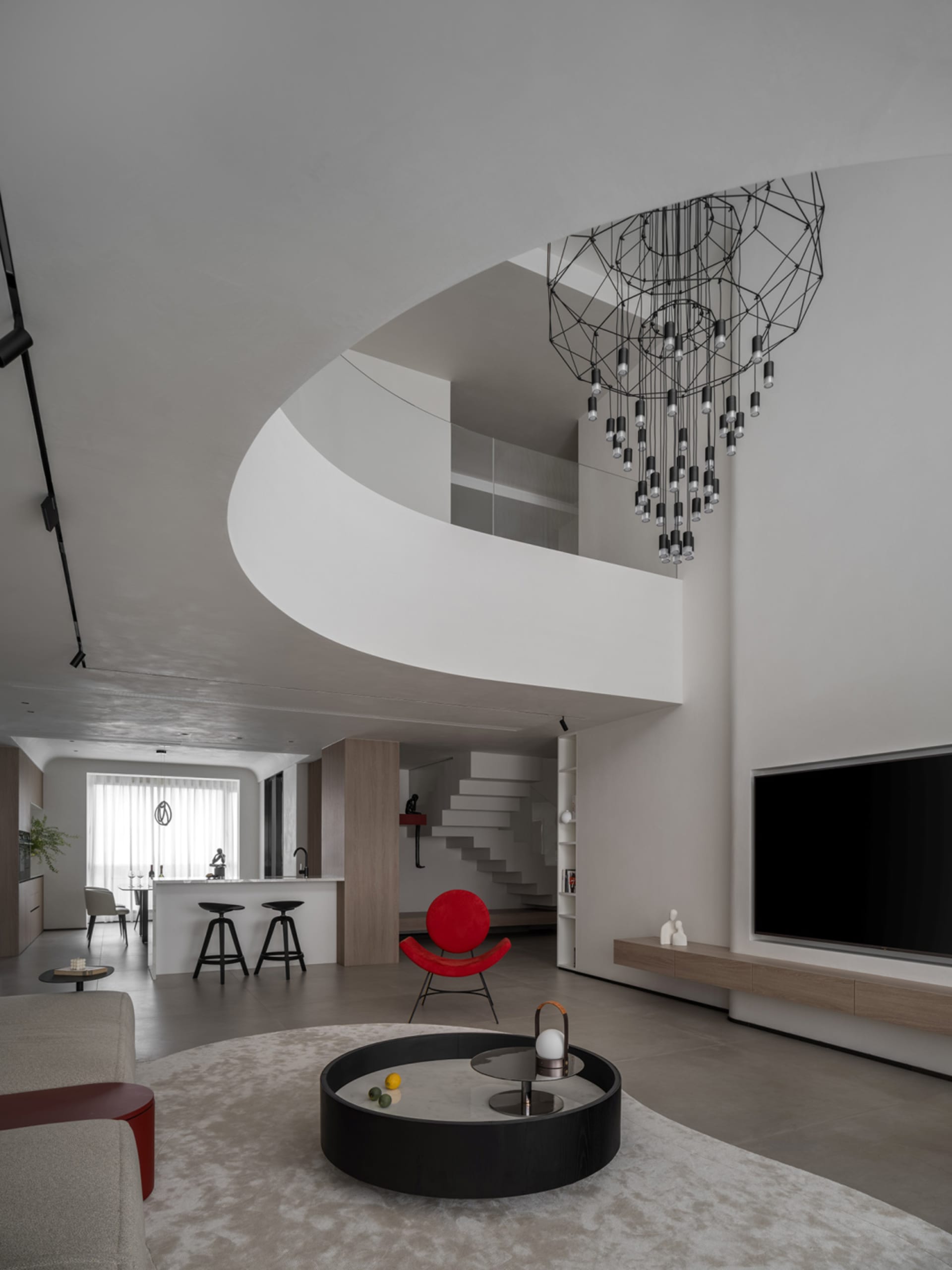 A modern living room with minimalist decor, featuring a red armchair, round black coffee table, and geometric chandelier.