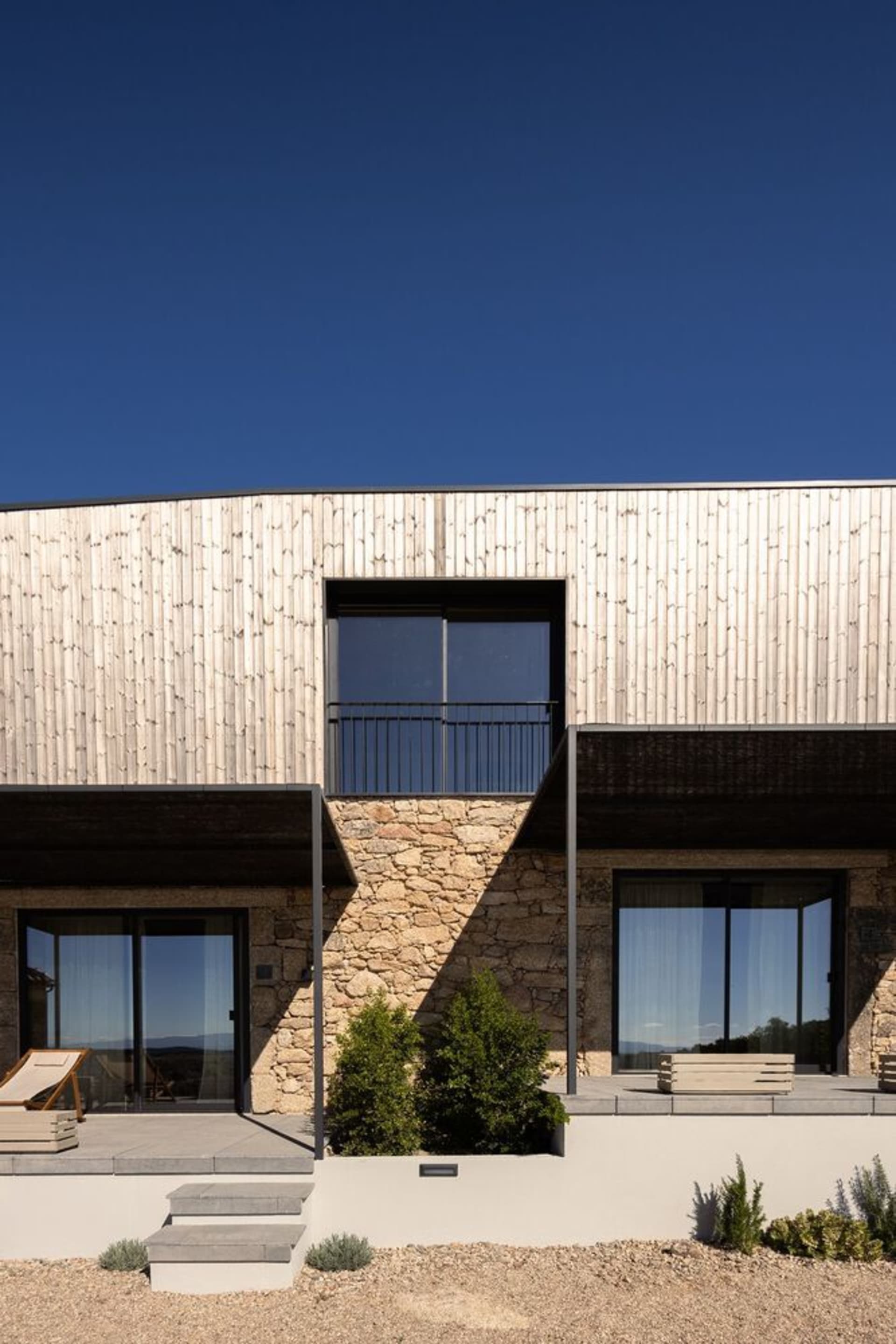 Modern residential exterior featuring minimalist design with wood cladding and stone foundation