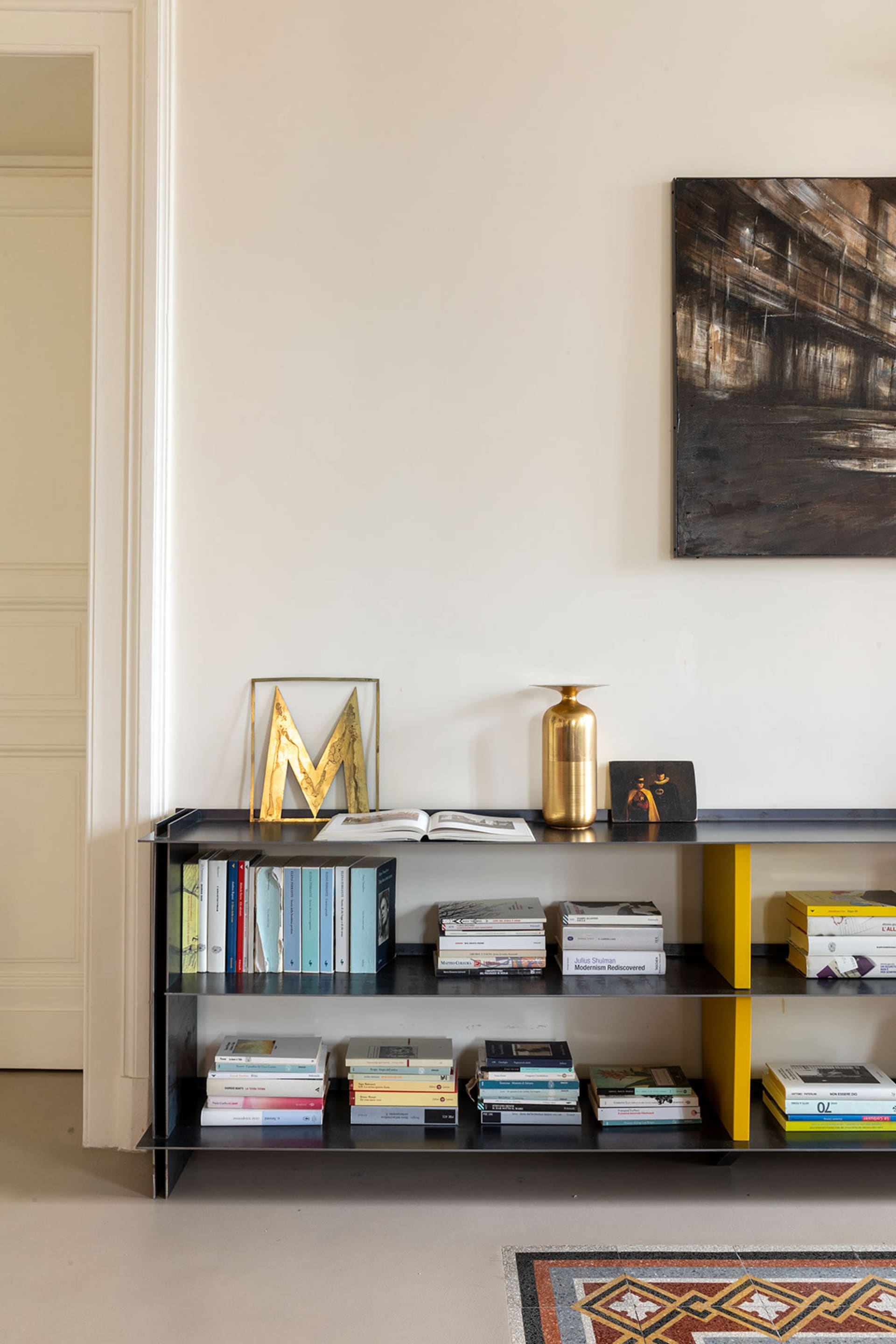 A modern metal shelf with books and golden decorative items against a white wall.