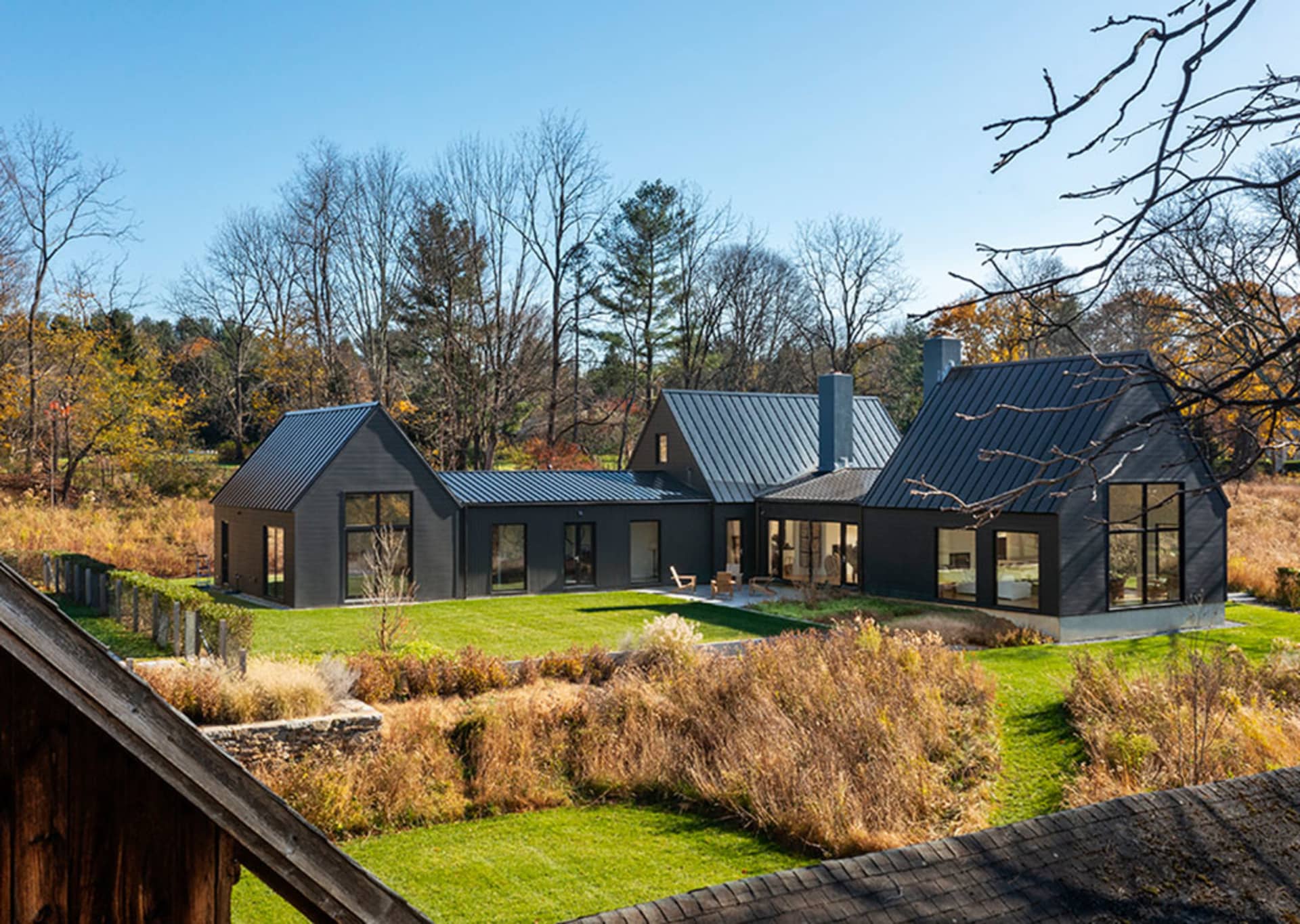 A modern farmhouse exterior with a metal roof, surrounded by a green lawn and autumn foliage.
