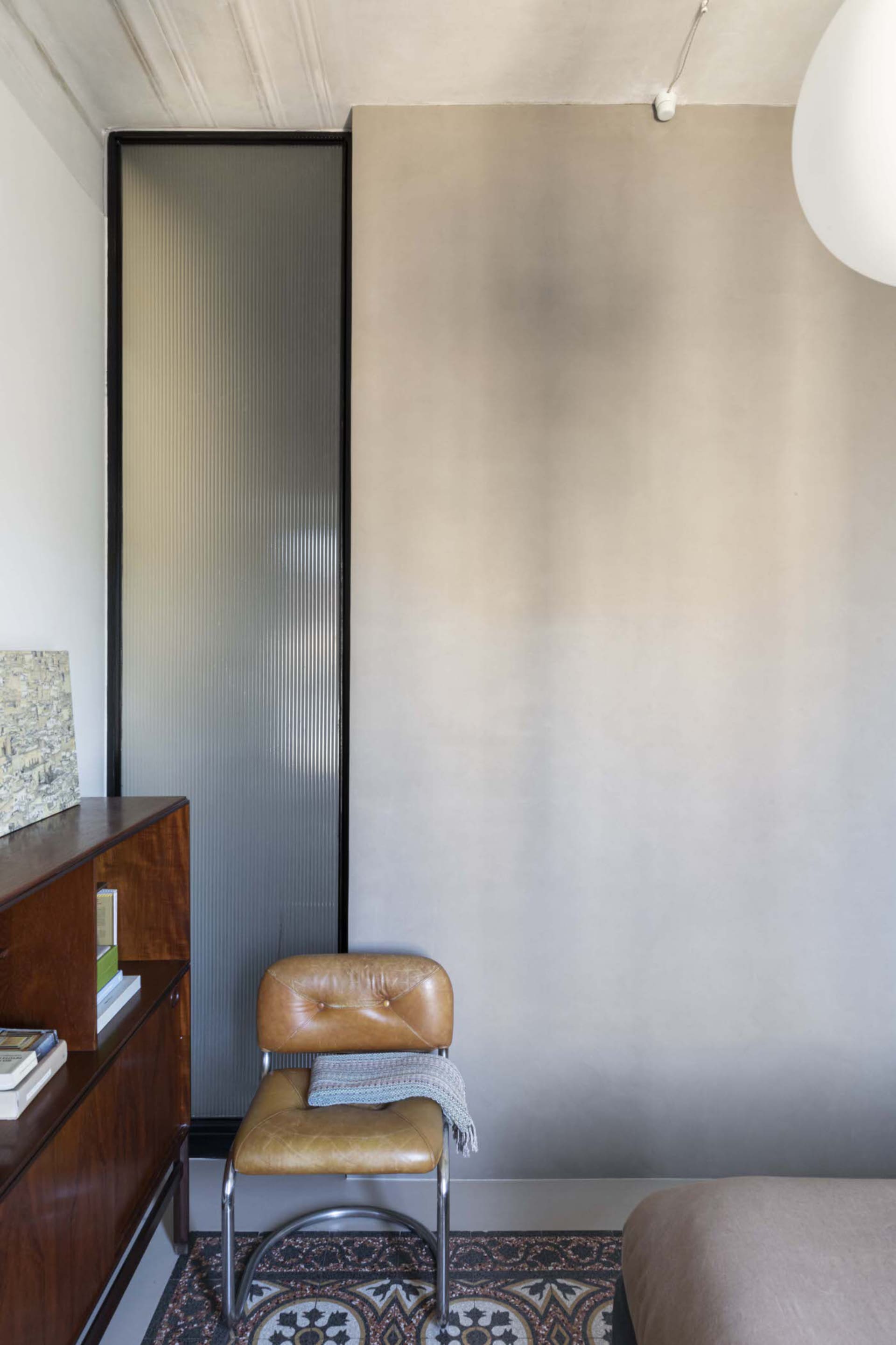 A modern minimalist interior with a concrete wall, brown leather chair, and tiled floor.