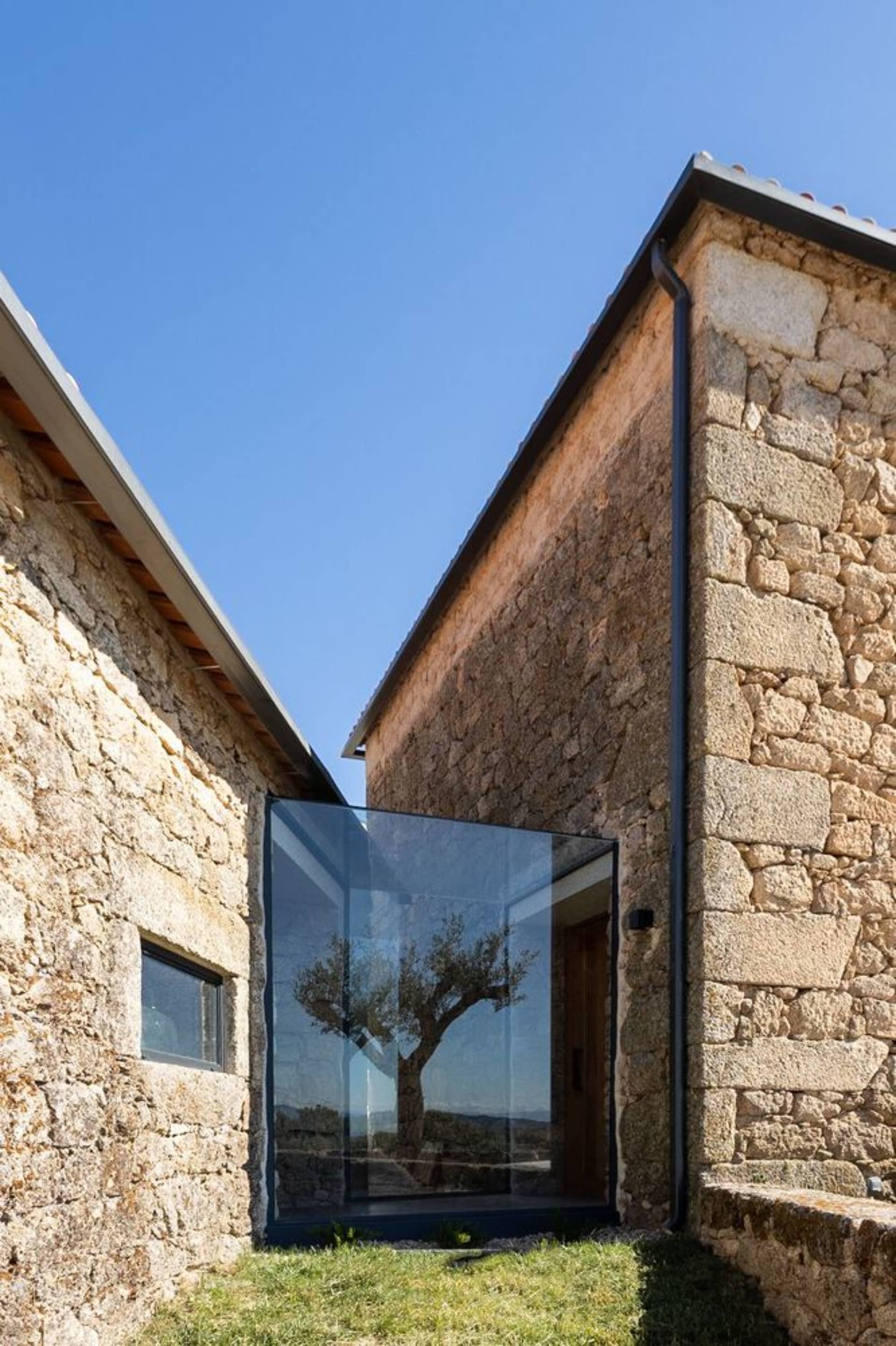 A modern stone house with large glass window and rustic exterior.