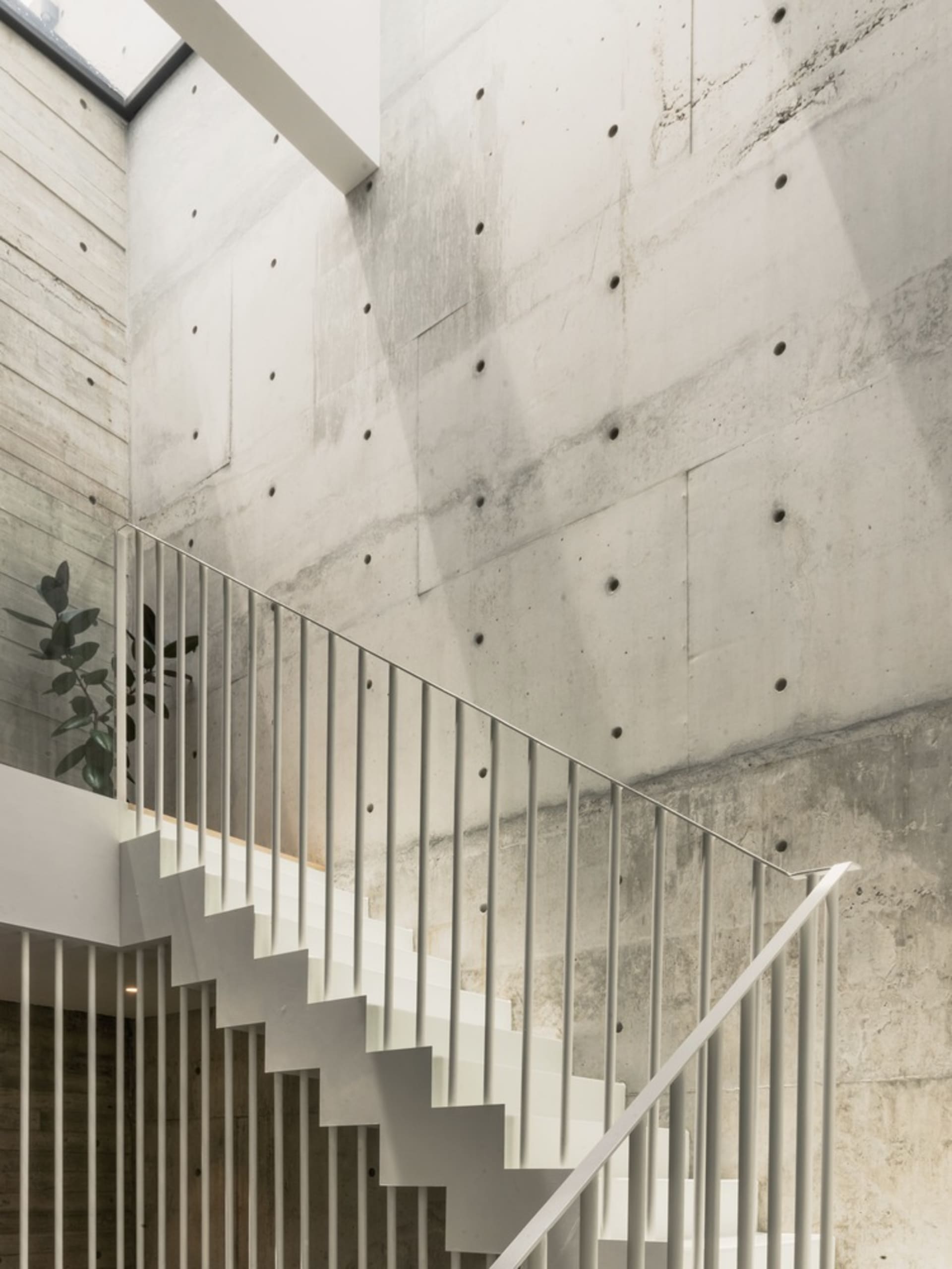A minimalist staircase made of concrete, featuring white railings against a raw concrete wall.
