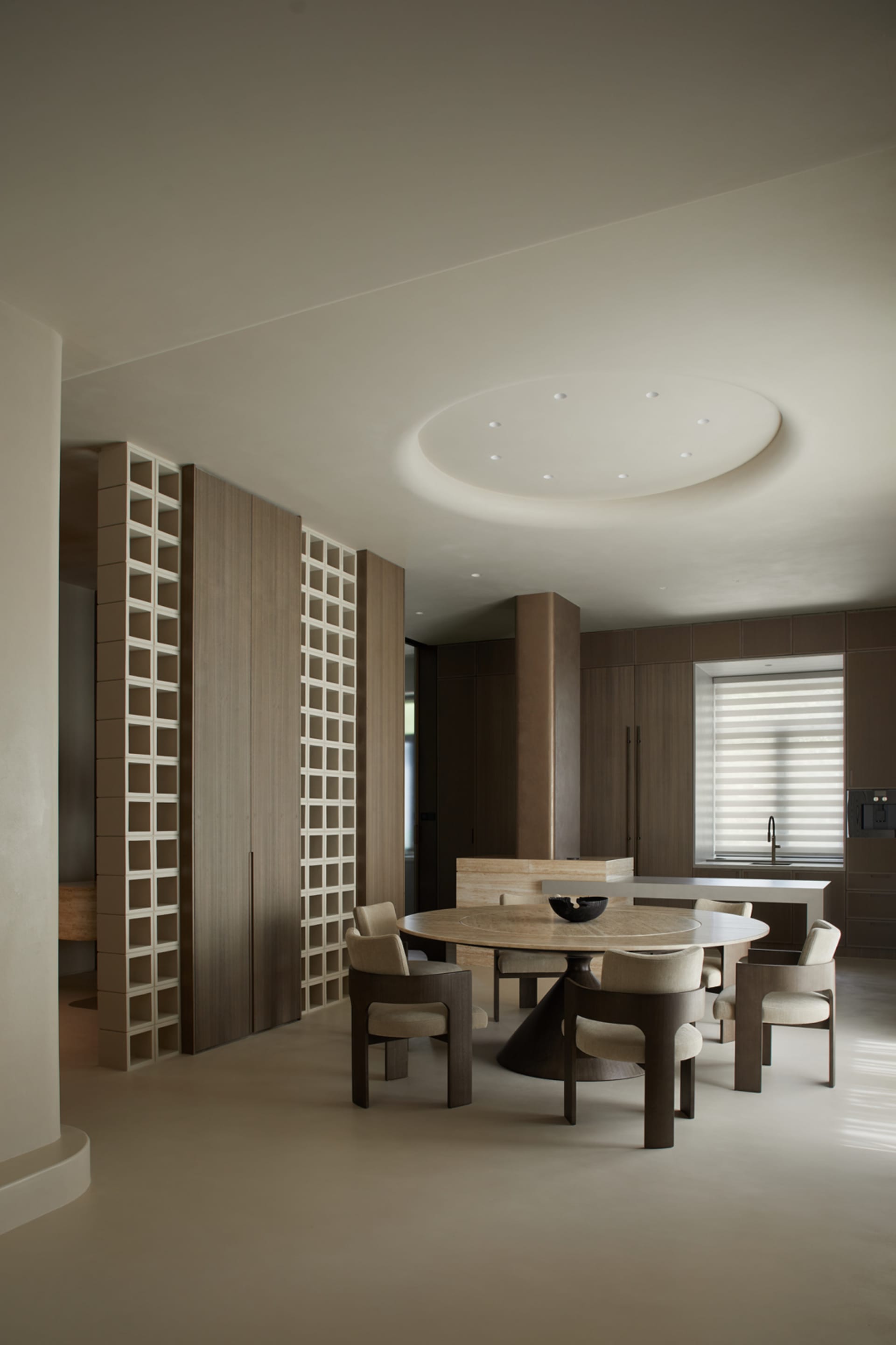 A modern minimalist kitchen with a circular dining table, wooden cabinets, and porcelain floor tiles.