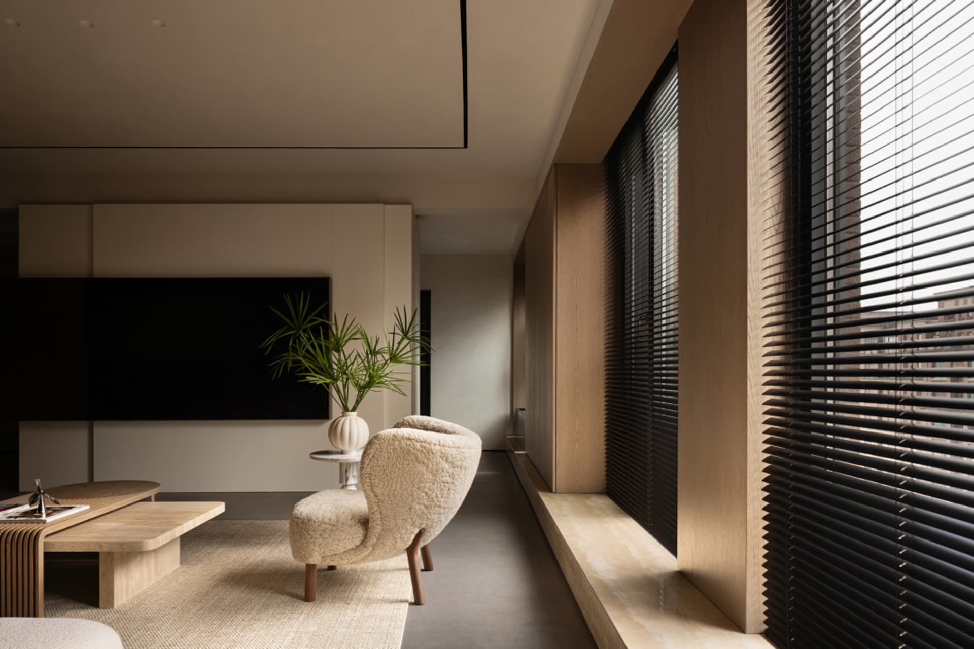 A modern minimalist living room featuring a beige armchair and a wooden coffee table, illuminated with natural light through