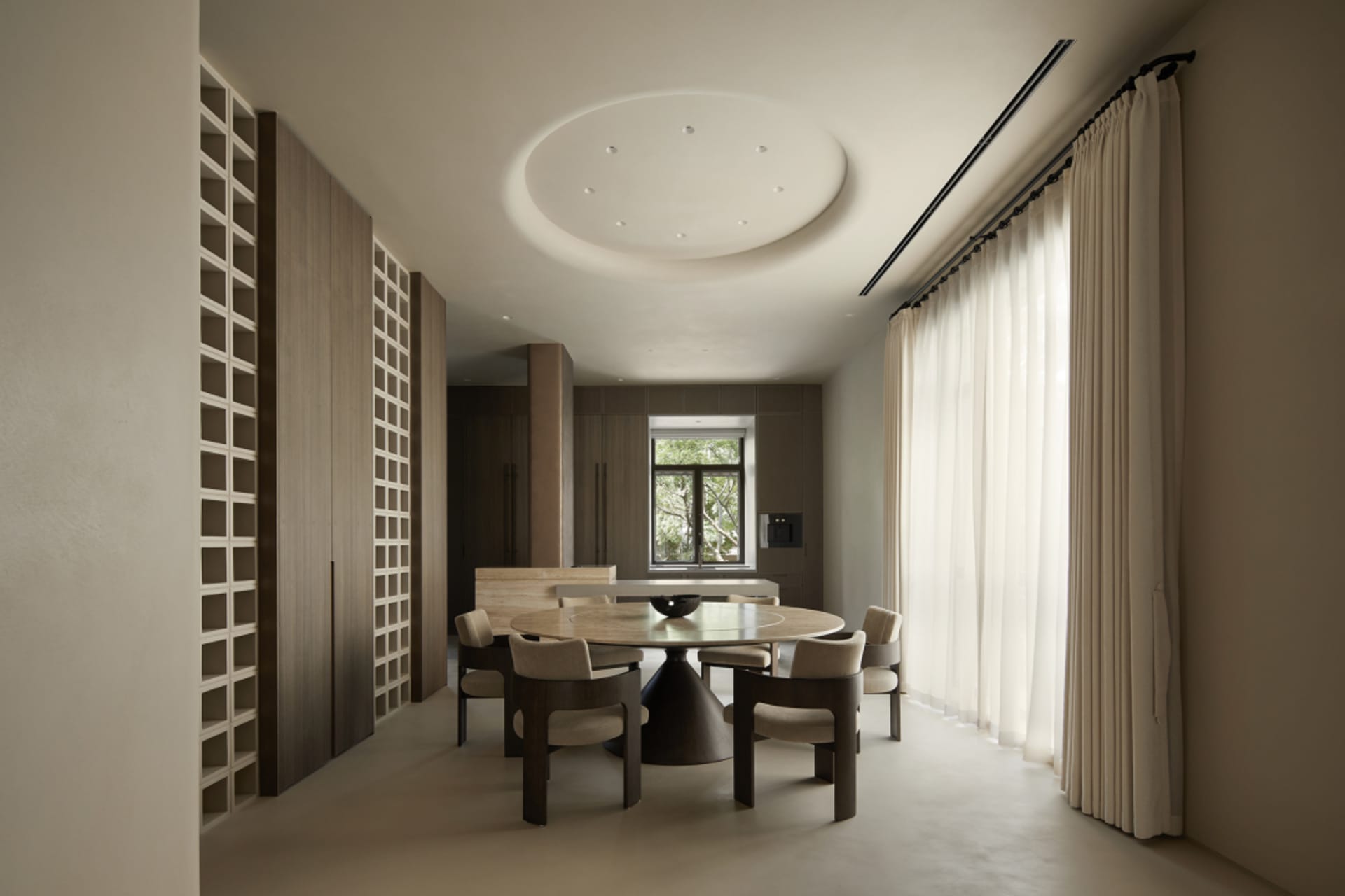 A modern residential dining room featuring a circular wooden table with marble top and matching chairs, surrounded by large w