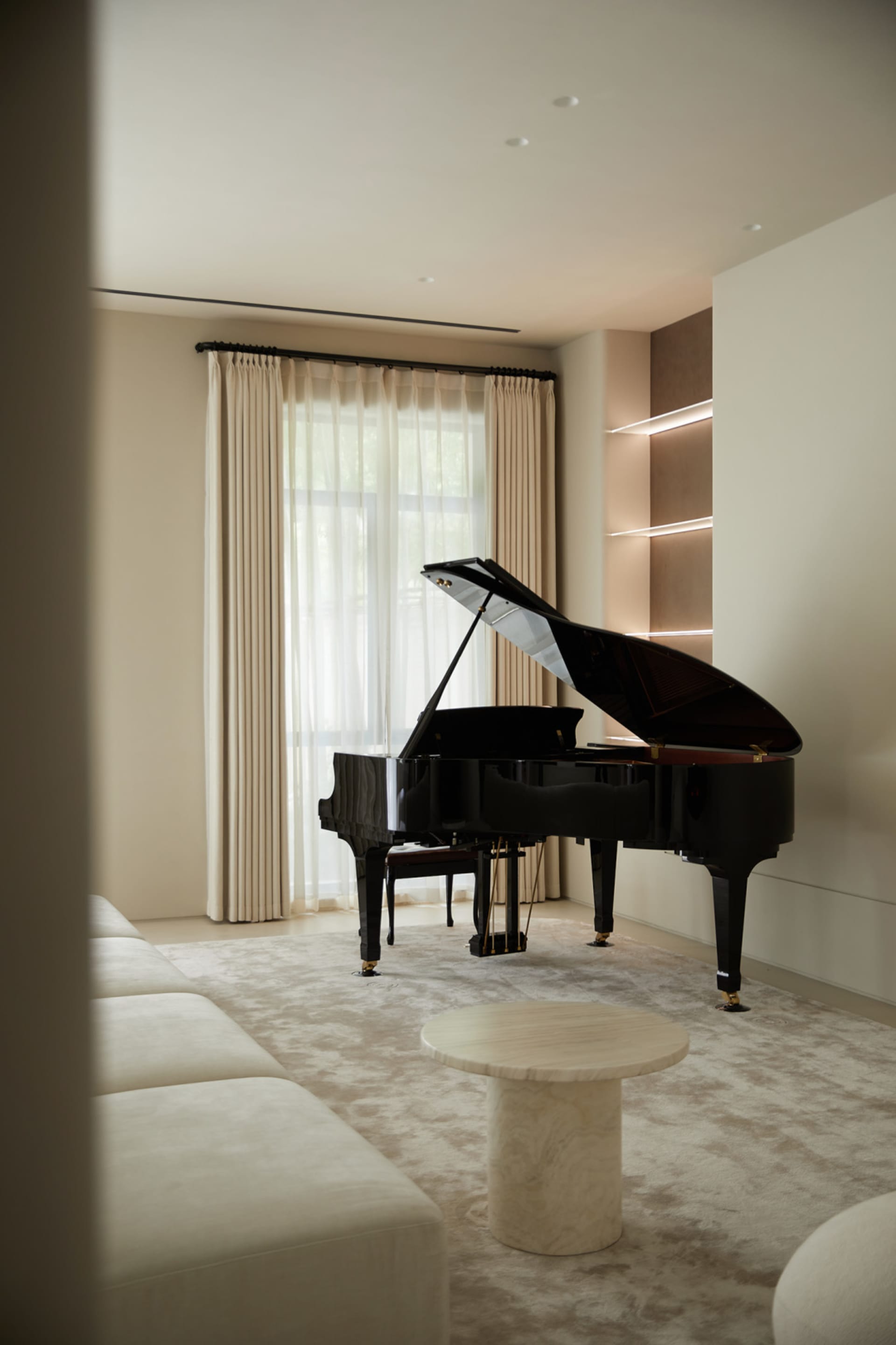 A modern piano room featuring a black grand piano, white leather sofa, white marble coffee table, and white curtains.