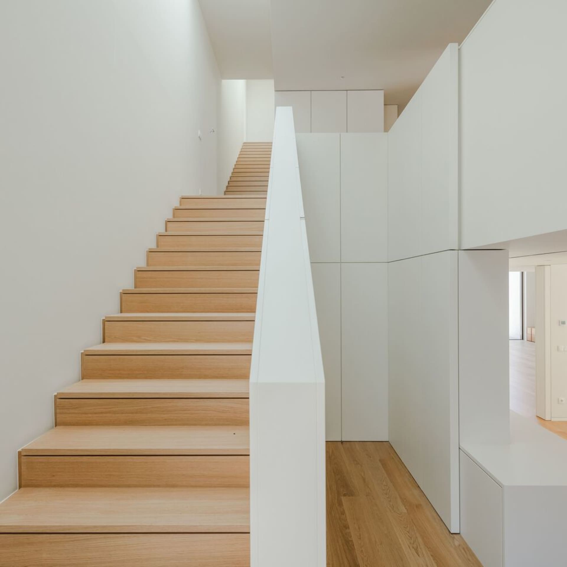 A minimalist staircase with wooden steps against white walls.