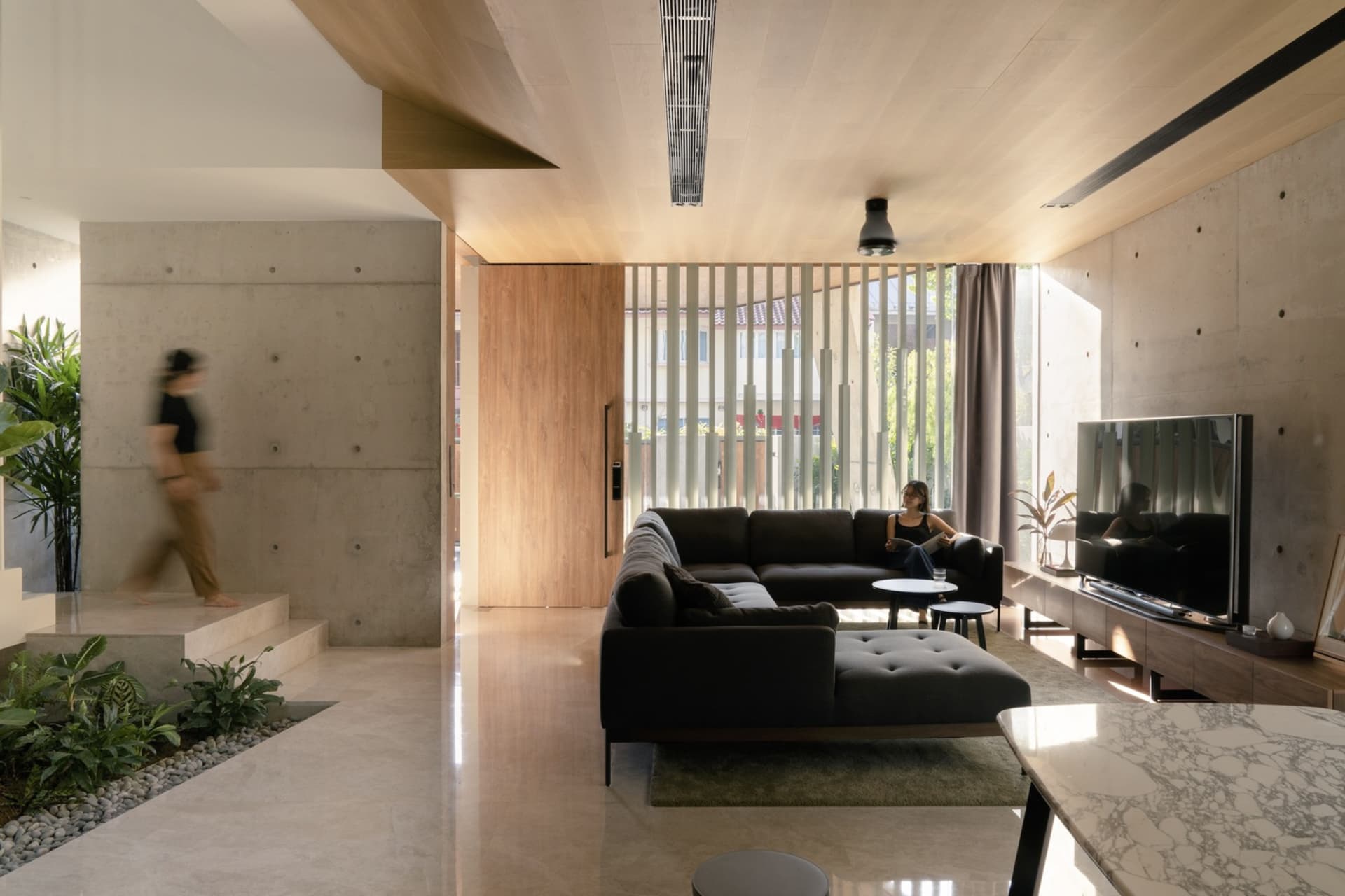 A modern living room featuring a concrete and wood interior design with a concrete floor, large windows, and a comfortable se
