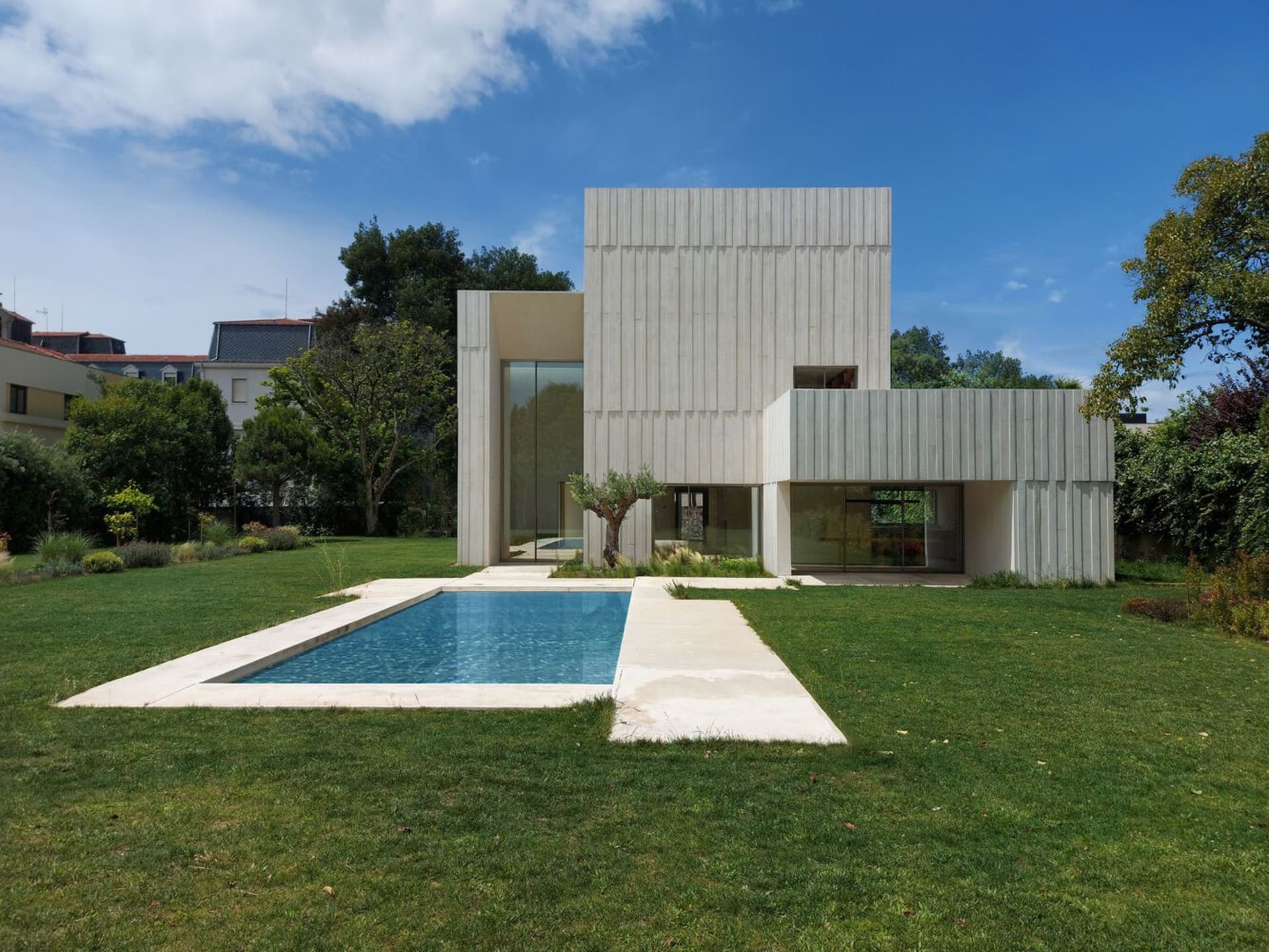 A modern house with a concrete facade and a swimming pool in the backyard with green grass.