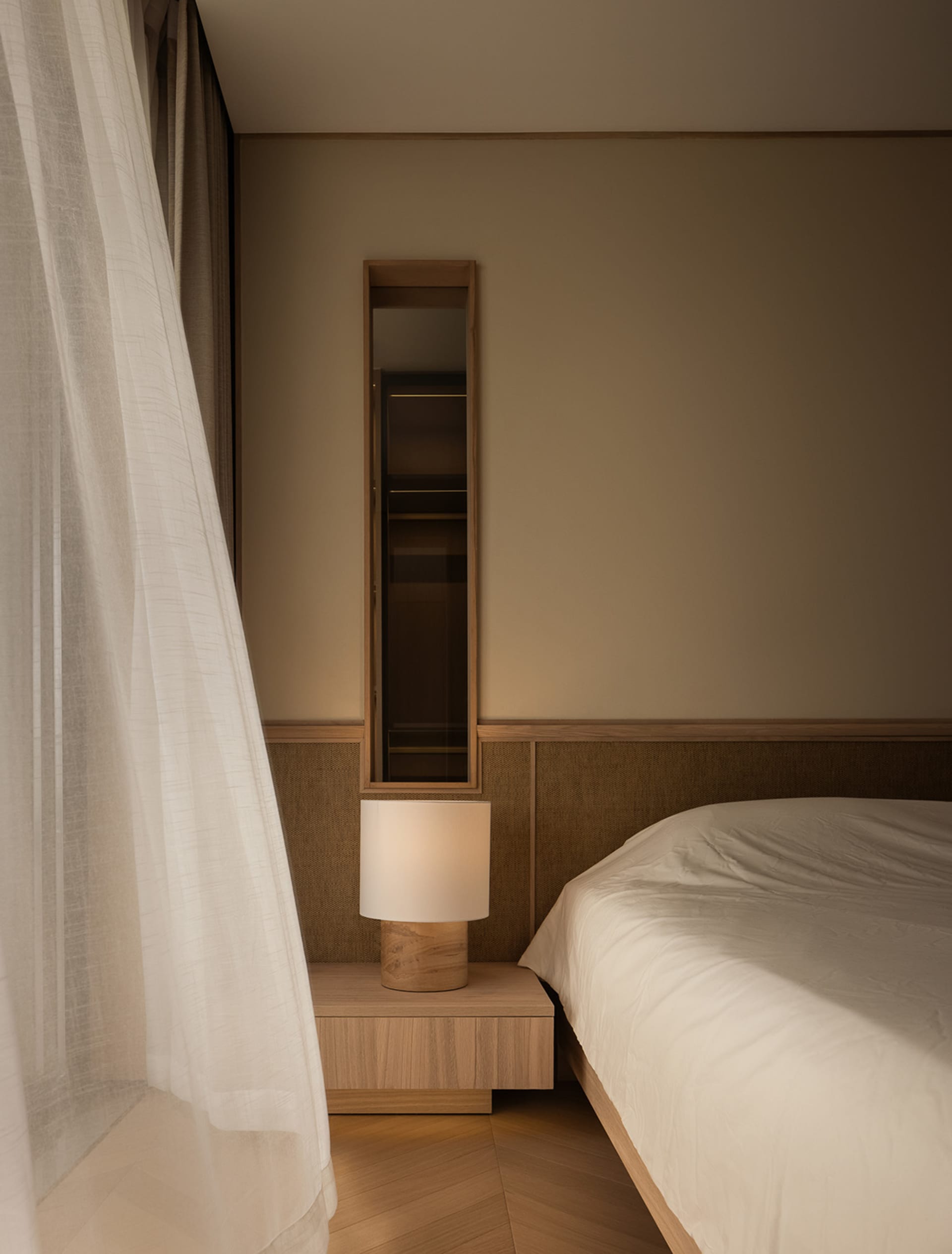 A minimalist bedroom featuring a wooden nightstand with a soft textile lampshade.