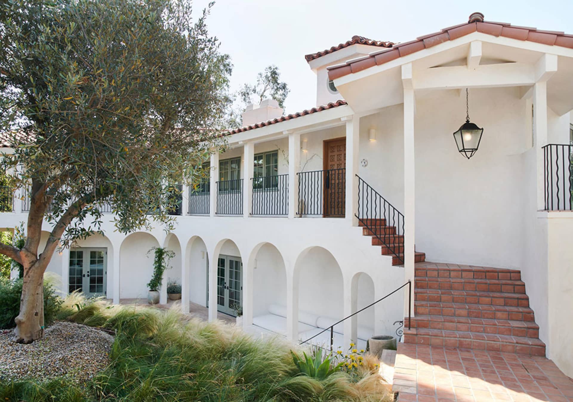 Stucco and terracotta exterior of a renovated Spanish-style home with white arches and terracotta roof tiles.