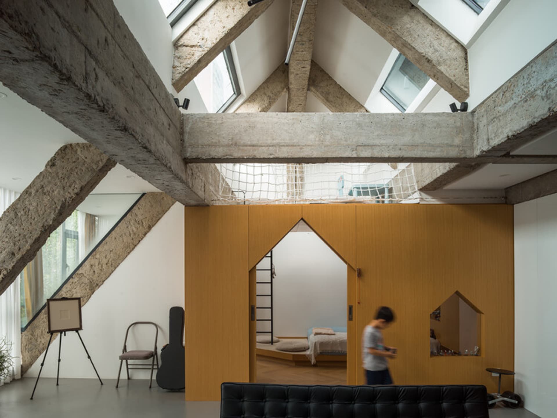 A modern industrial living room with concrete walls, exposed beams, and natural light from skylights.