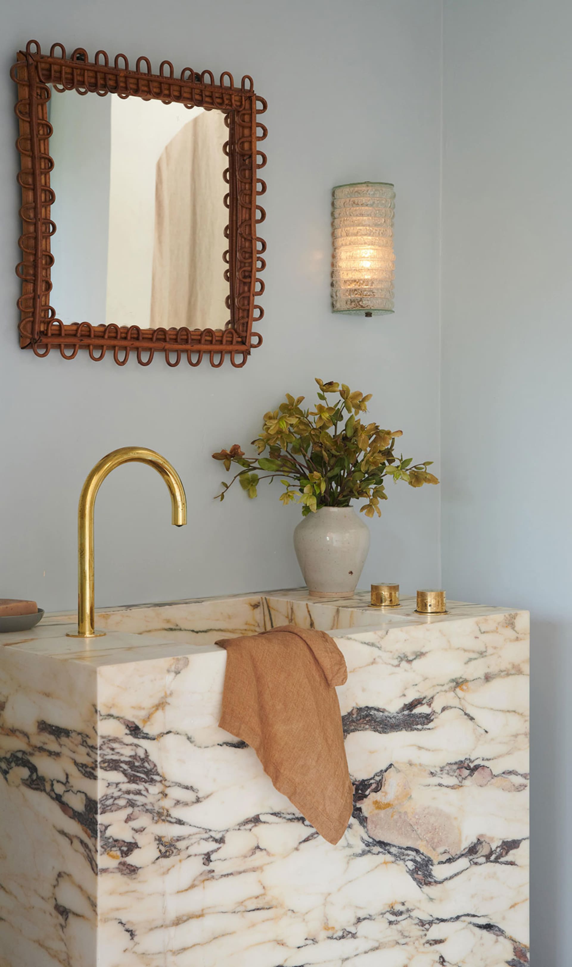 Modern bathroom with a marble countertop, brass faucet, and decorative vase with flowers.