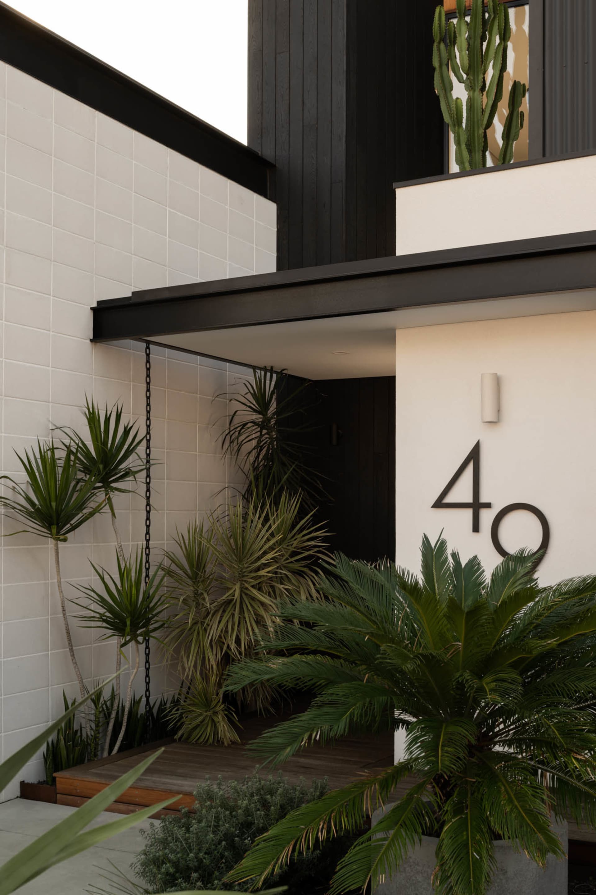 Modern front door entryway featuring concrete, wood, and lush green plants