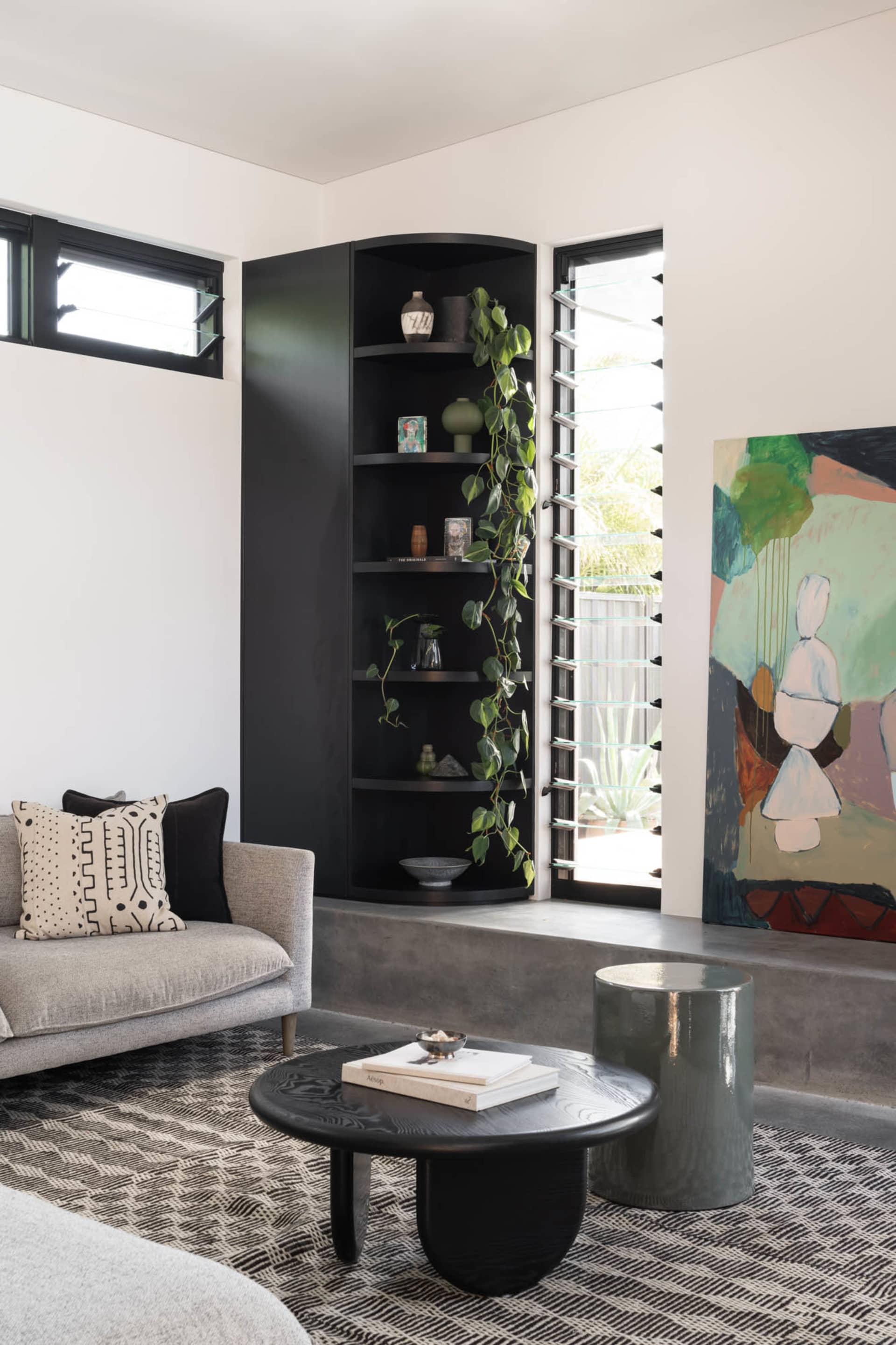 A modern living room featuring concrete walls and plants in corner planters.