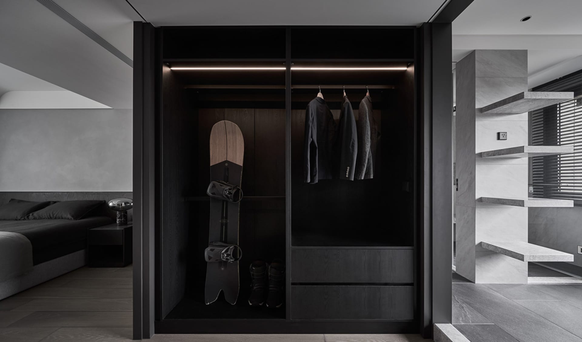 Modern minimalist black closet with a snowboard, jackets, and shoes on a wooden surface.