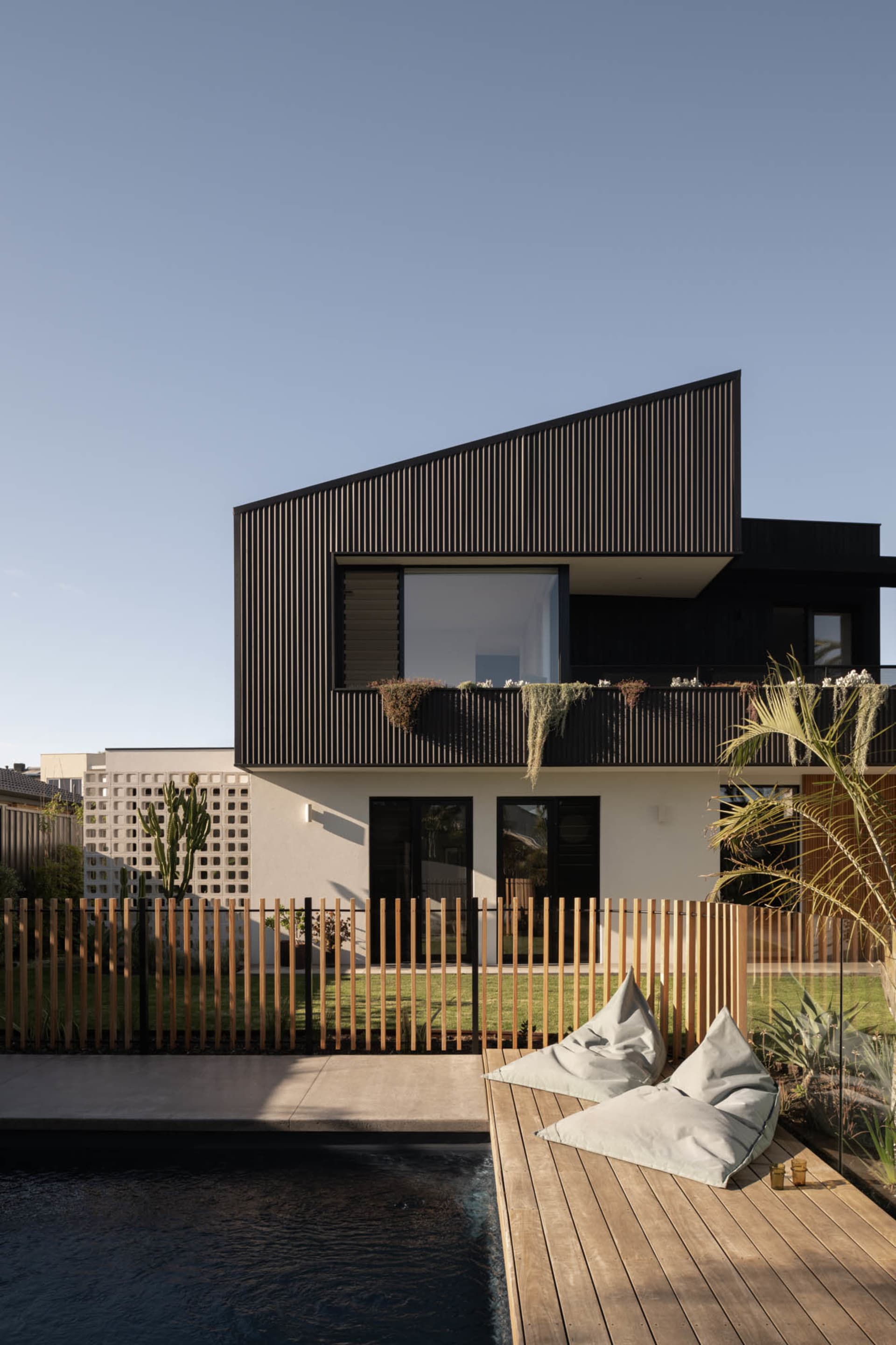 Modern beach house with wooden deck and glass fence surrounding a concrete pool.