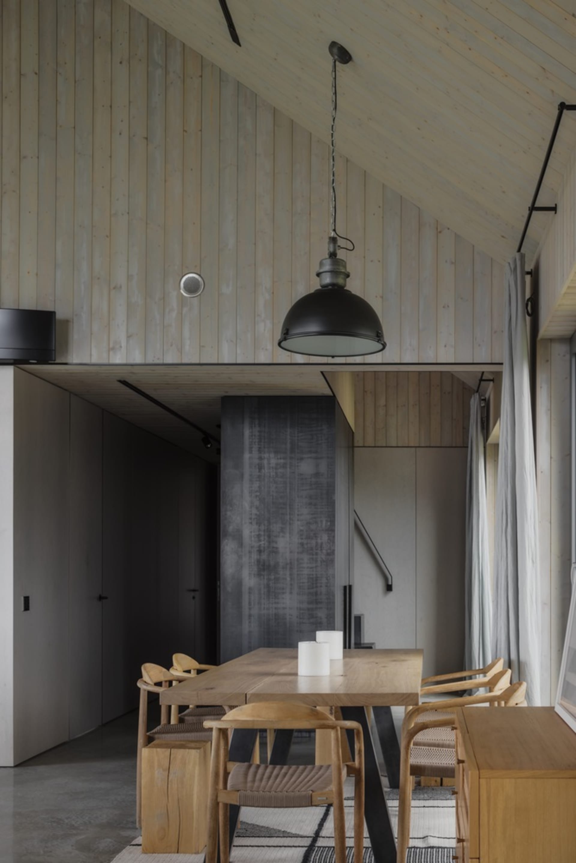 A modern dining room with wooden furniture, featuring a wooden table, chairs, and pendant light.