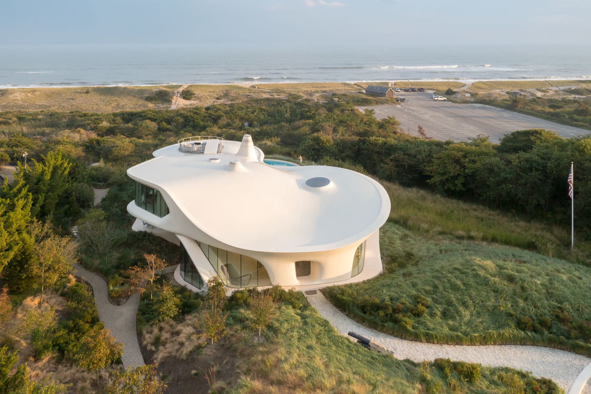 A modern, white stucco and glass residential house with a curved roof and a pool.