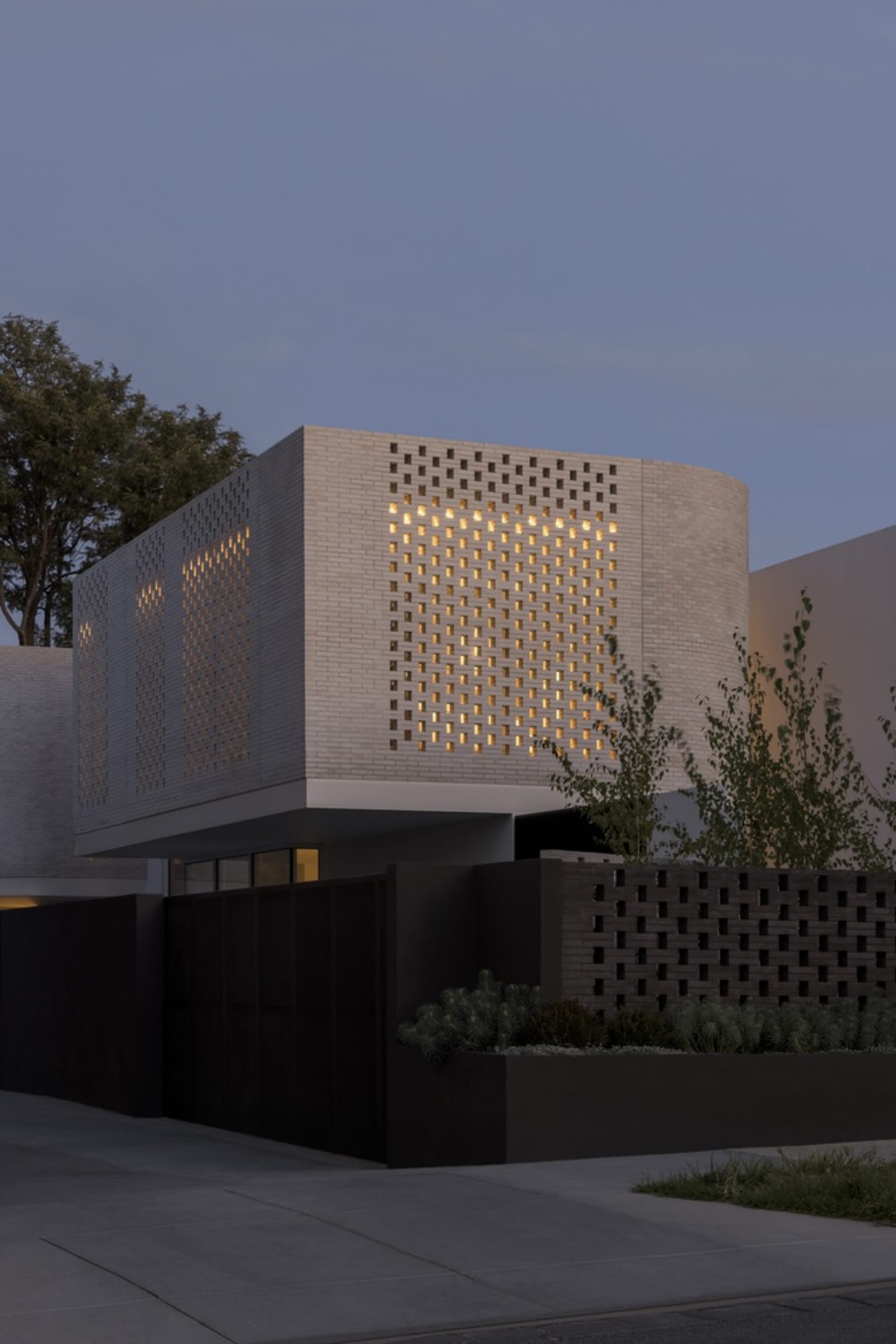 Modern house exterior with a brick wall featuring a perforated pattern and illuminated lights.