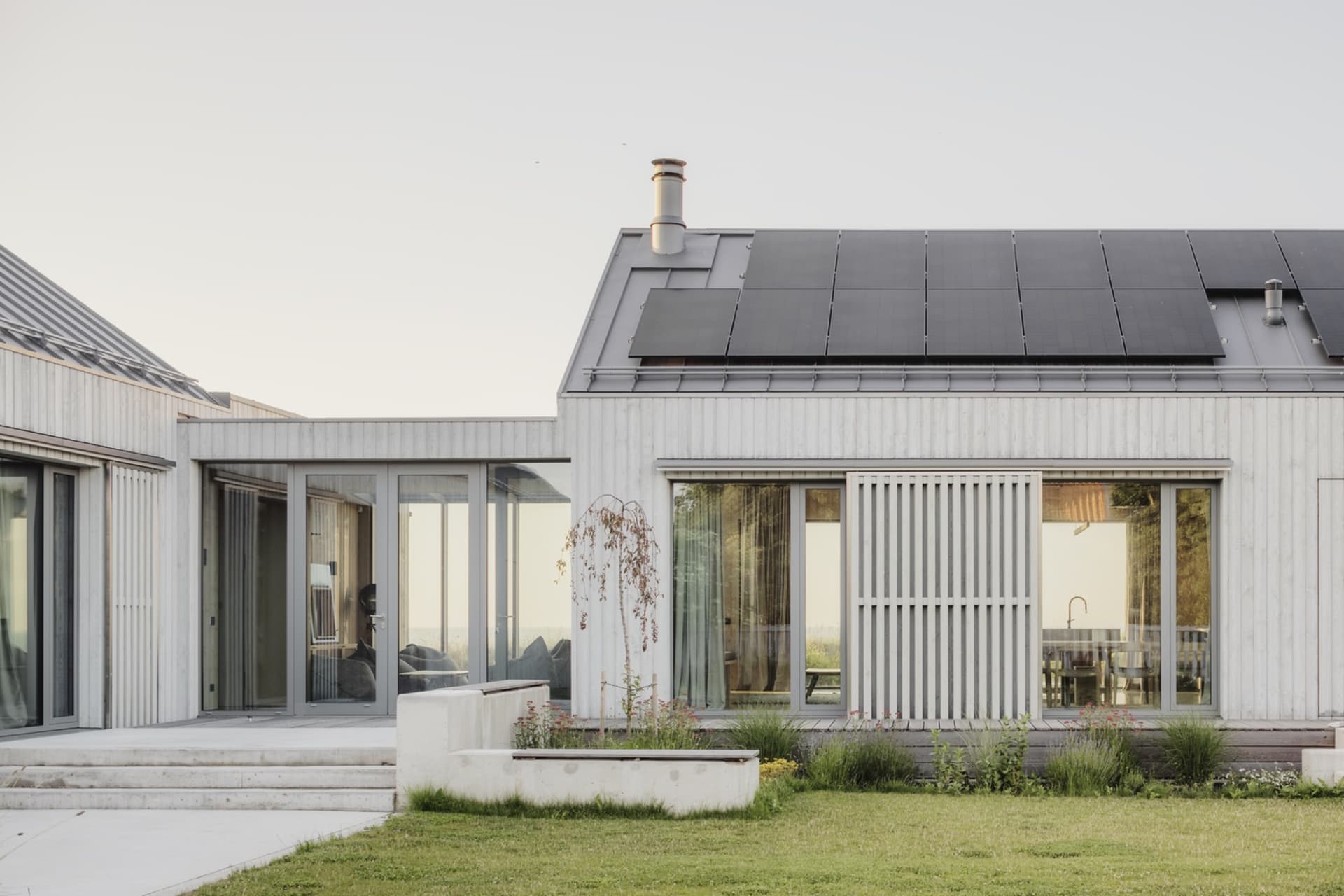 Modern residential building with rear yard featuring concrete deck and steps, solar panels on the roof, and green grass.