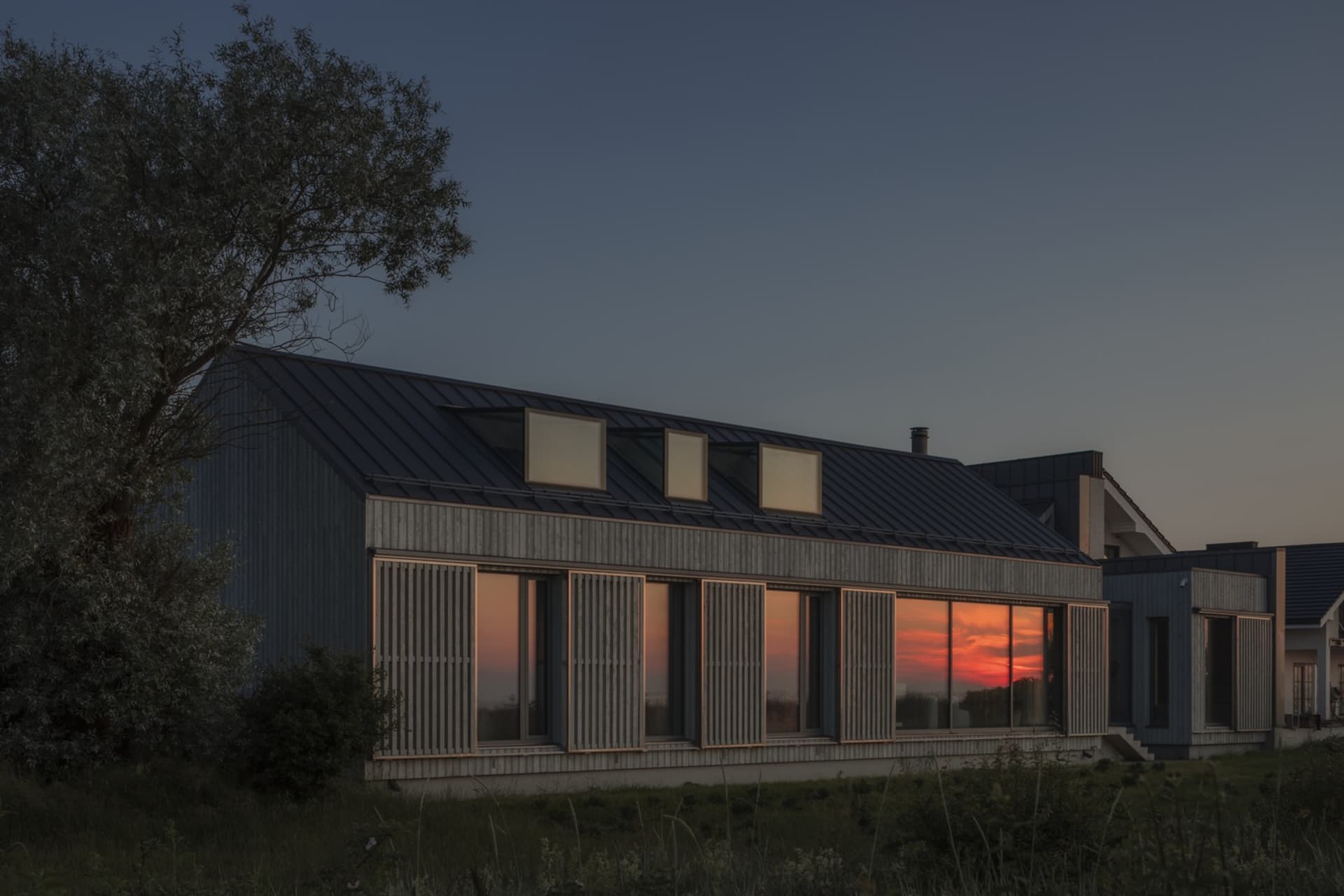 A modern house with metal cladding and large glass windows against a sunset sky.