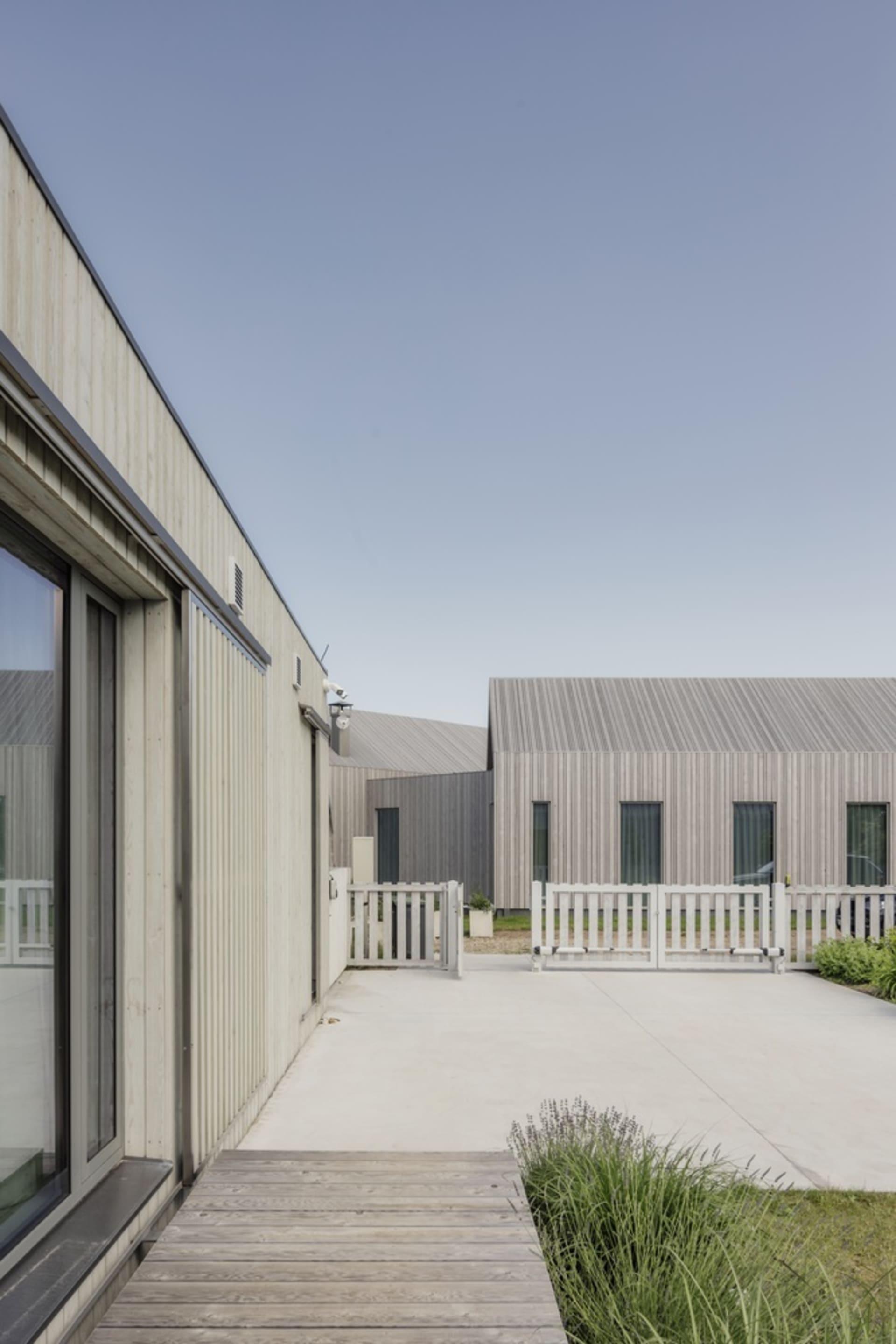 Modern residential exterior with wooden board and batten siding and a white picket fence.