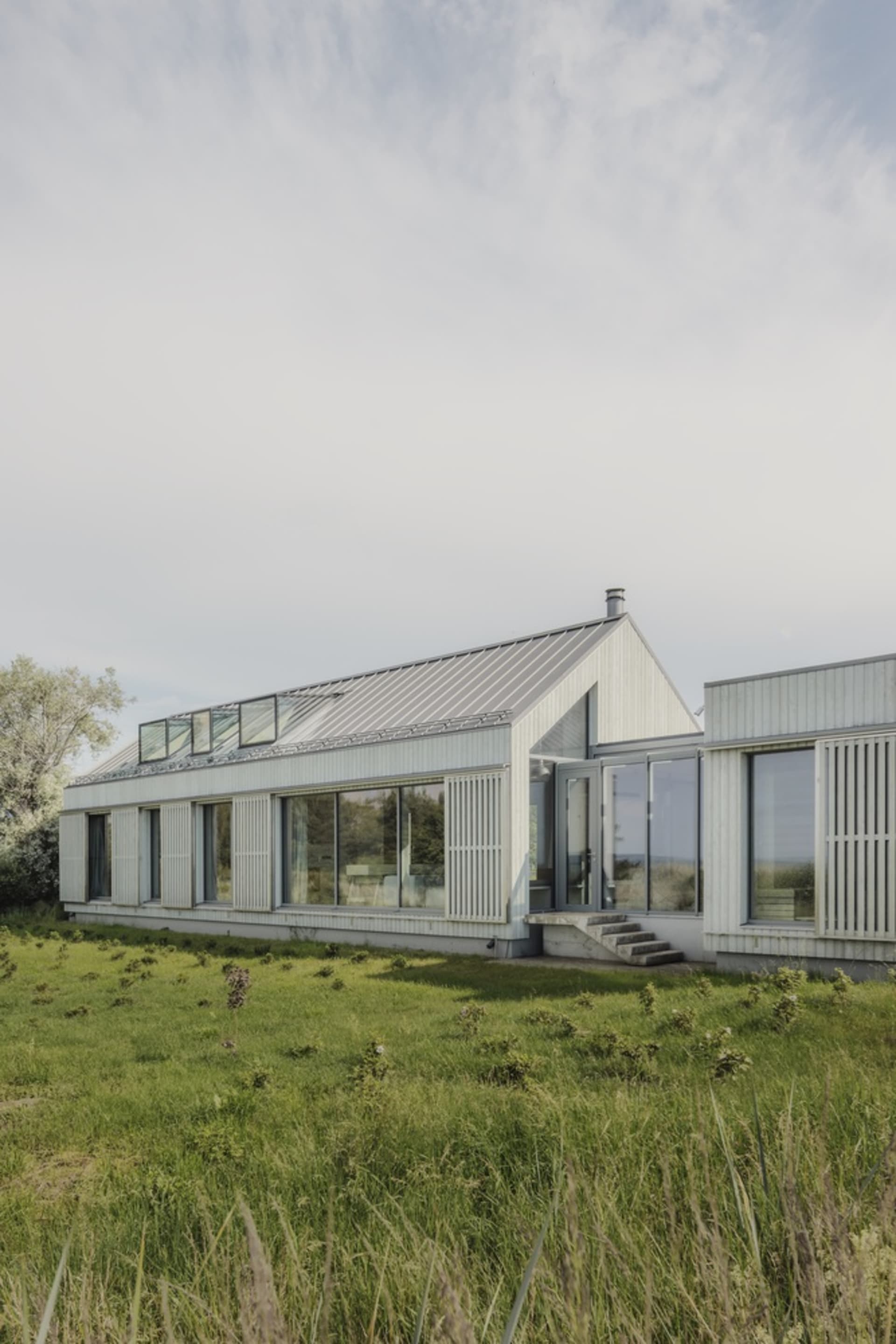 A modern residential house with glass walls and a metal-clad exterior.