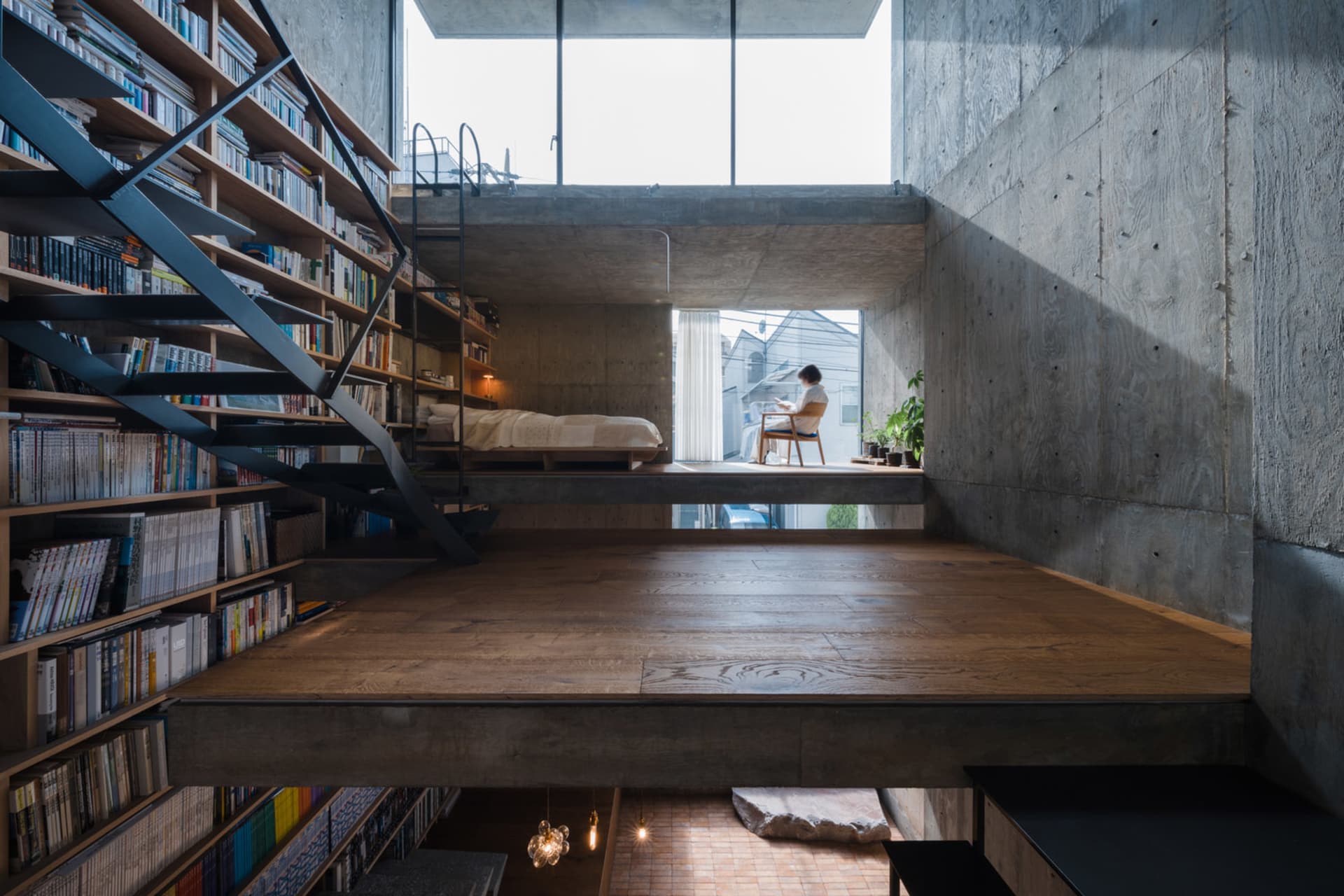 Minimalist residential interior featuring concrete and wood materials, with a person sitting at a window.