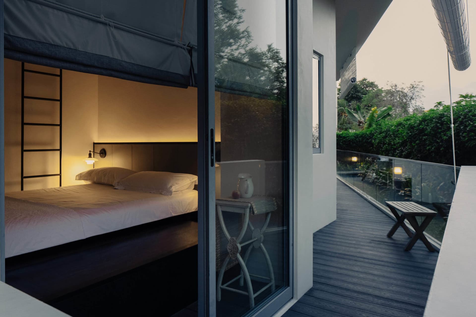 Modern minimalist bedroom with a double bed, glass door, and outdoor seating area.
