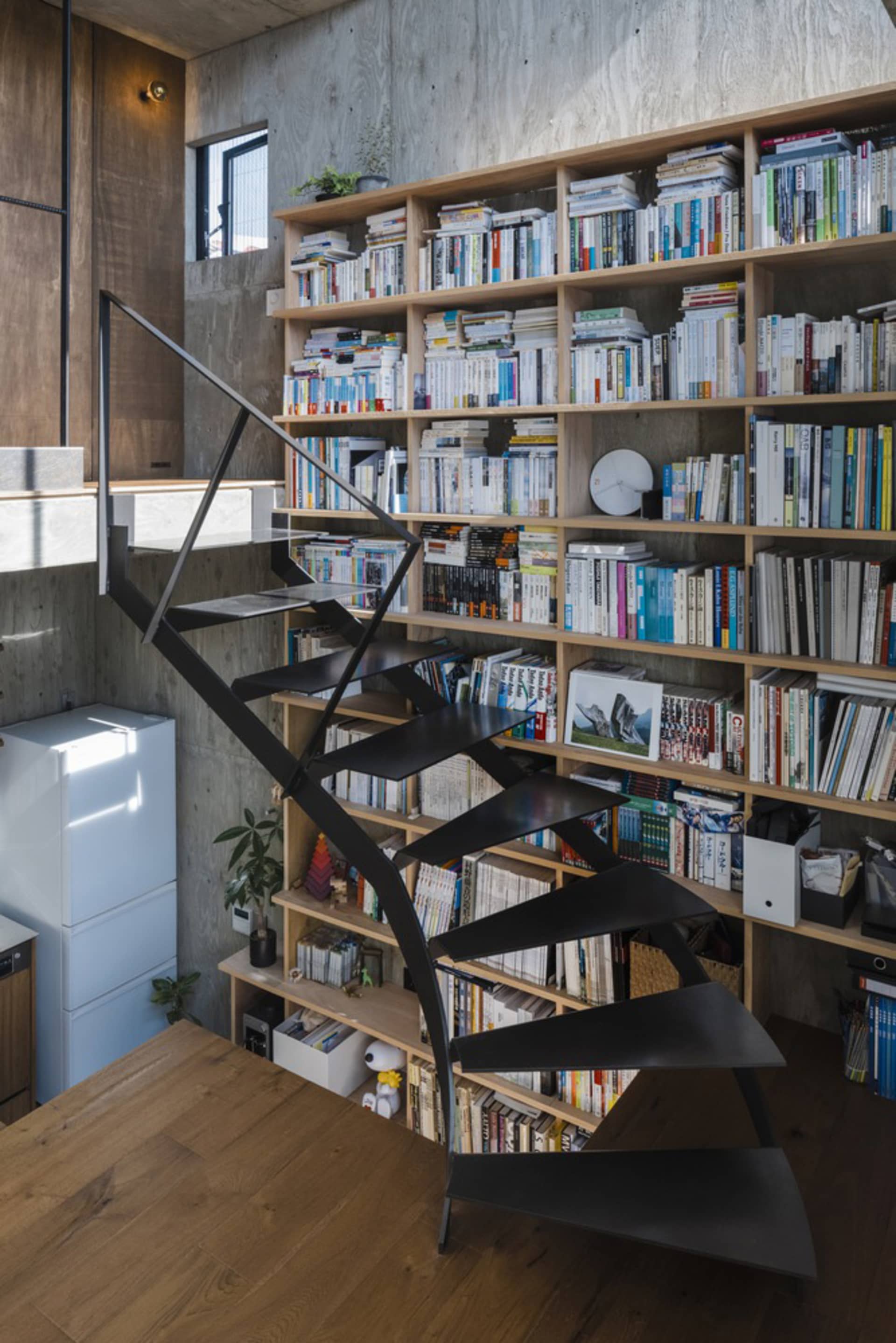 A modern interior design featuring a black staircase with an open railing, set against a background of wooden shelving filled